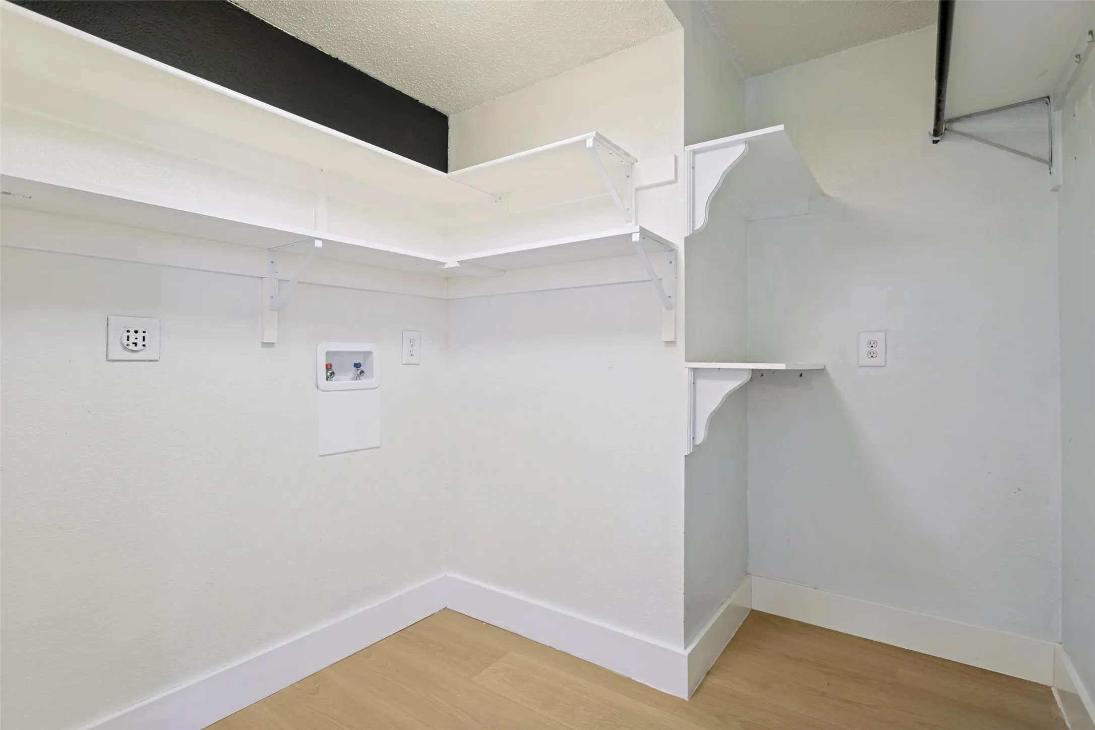 Utility area featuring wood-finish flooring and multiple white wall shelves