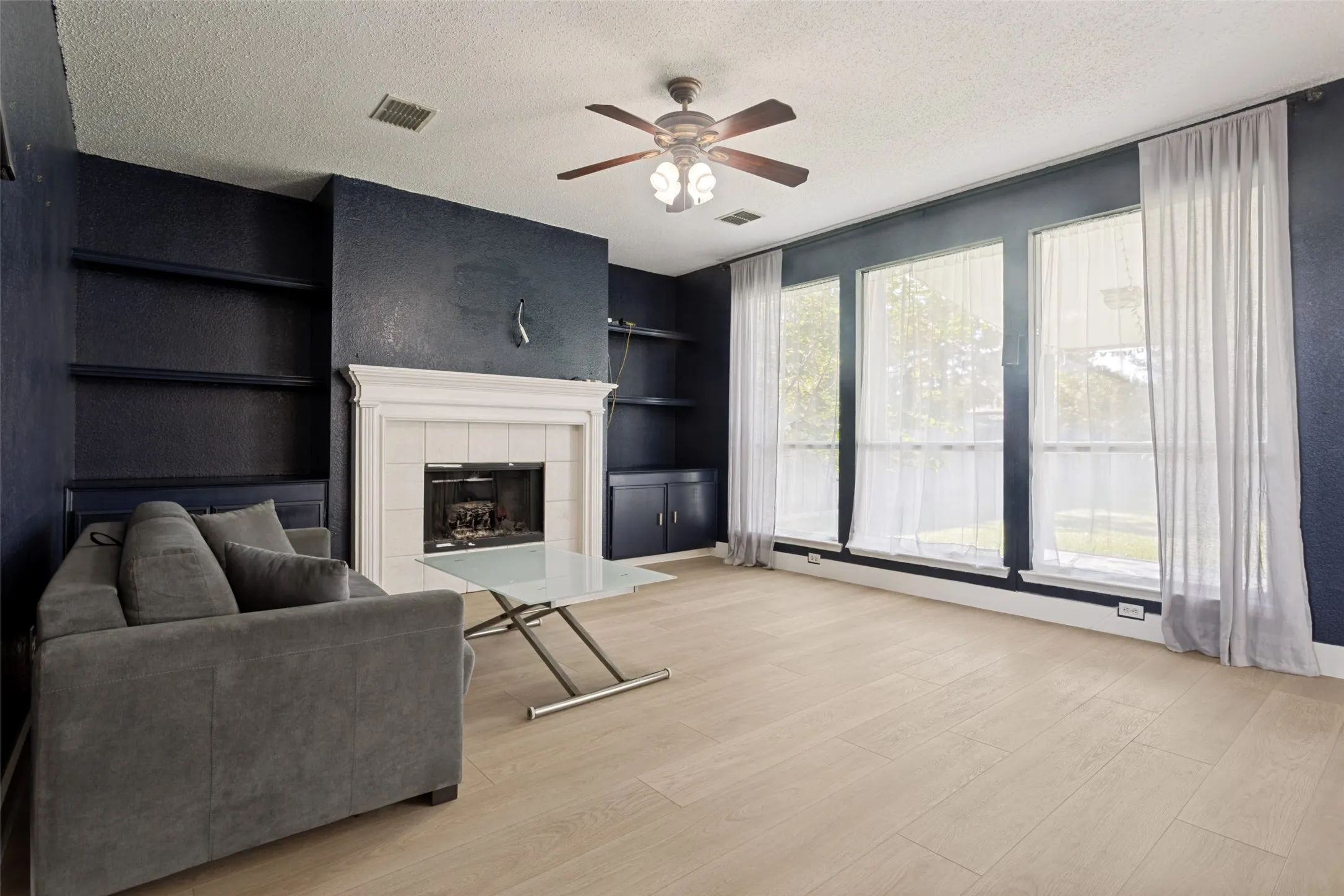 Living area featuring wood-finish flooring, a white mantel fireplace, and built-in shelving