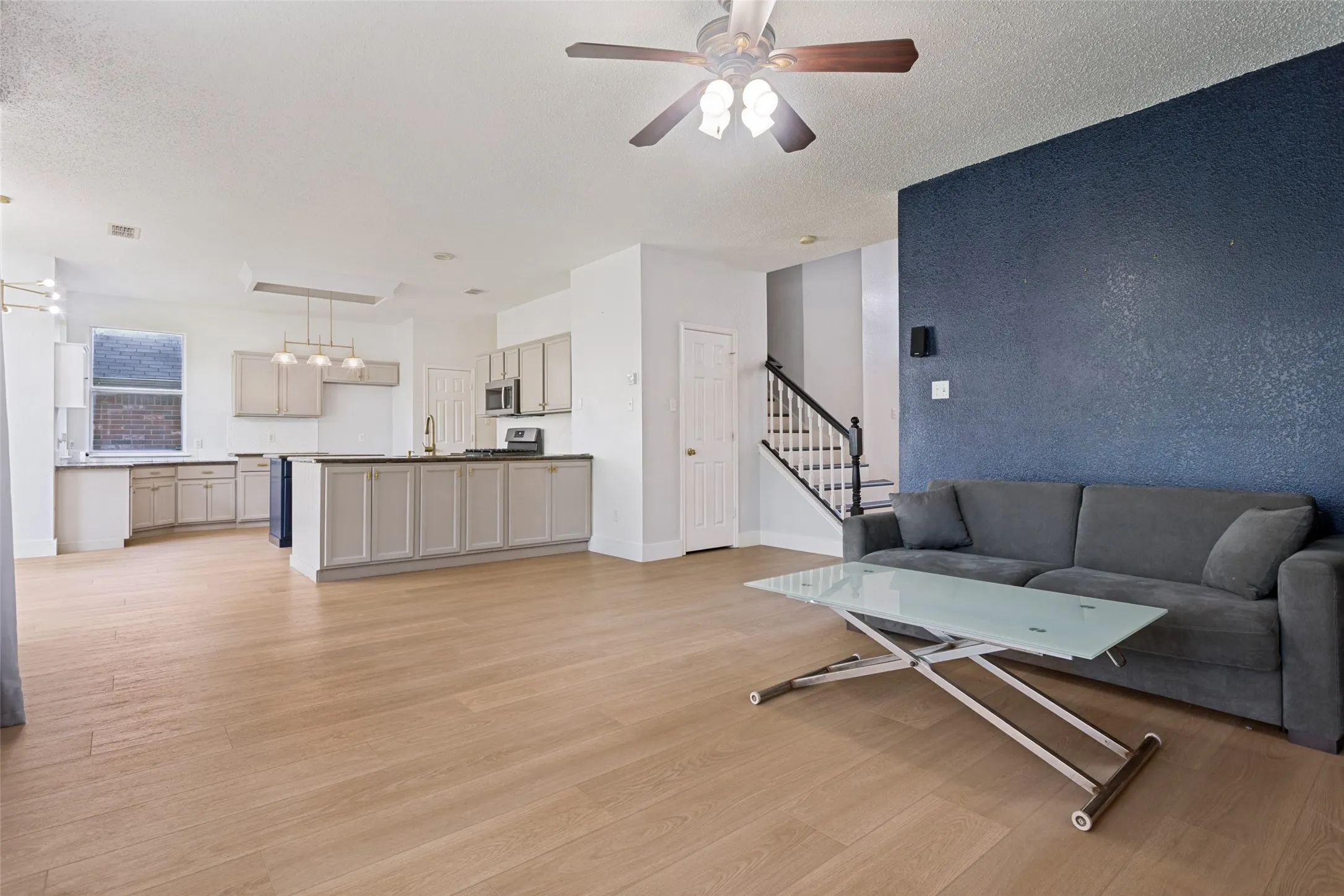 Spacious living area featuring light wood-finish flooring, a contemporary ceiling fan, and a striking accent wall