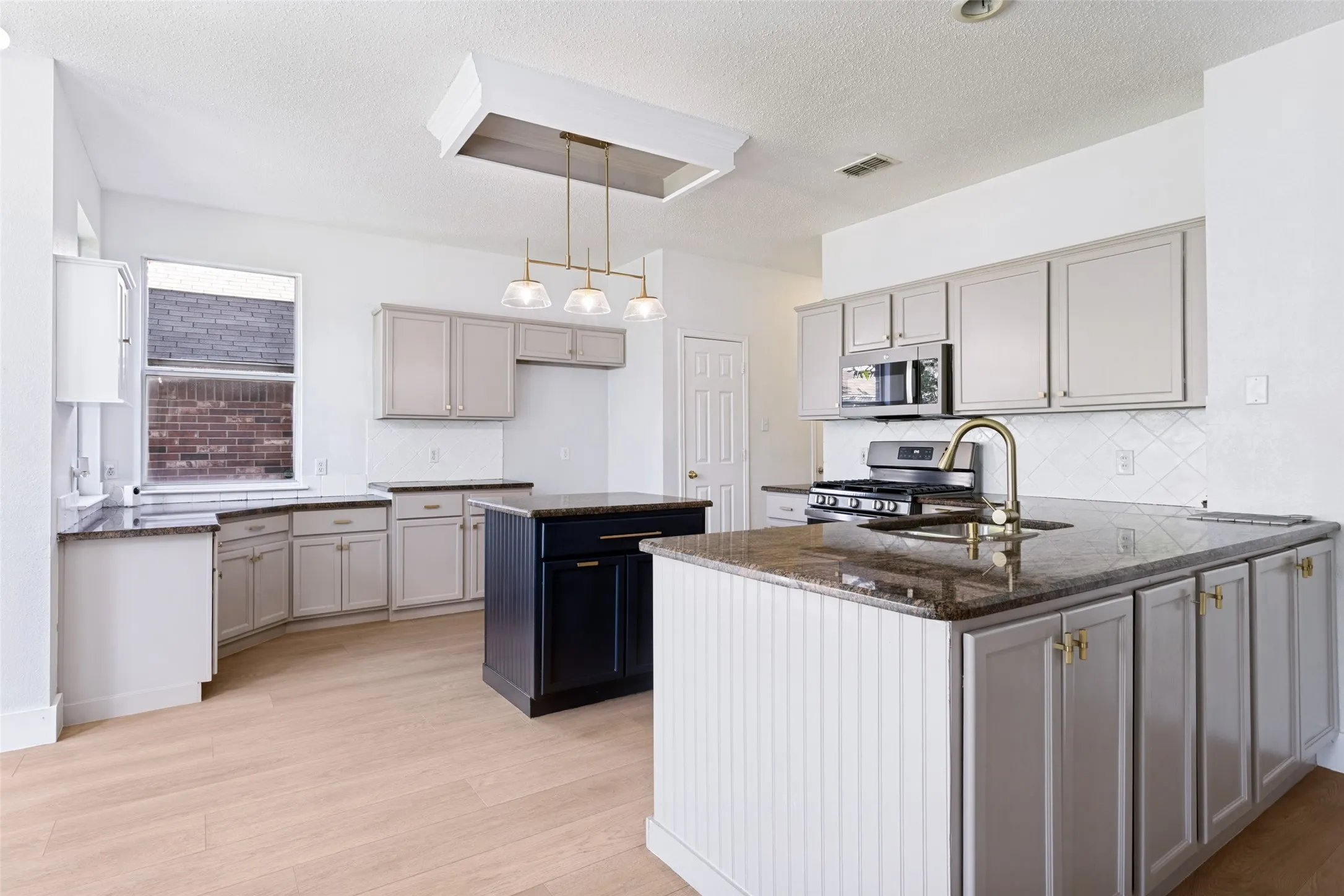 Kitchen featuring a multi-level island, light wood-finish flooring, a stainless steel gas range, and a brass-finish faucet