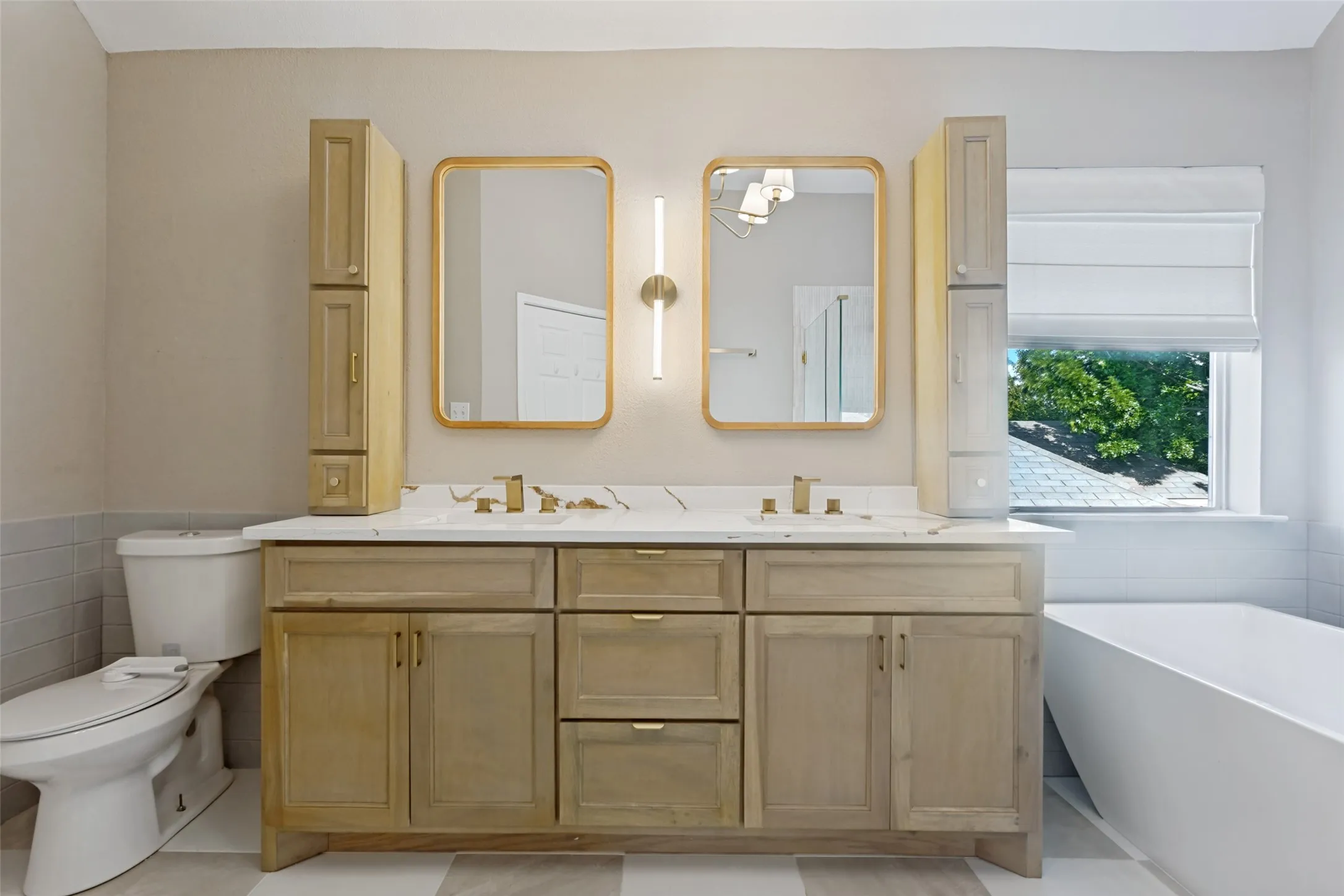 Dual vanity with light wood-finish cabinetry, white countertop, and gold-framed mirrors