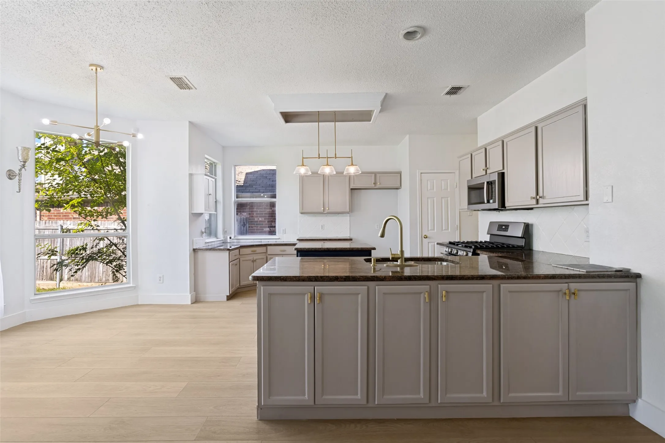 Open-concept kitchen featuring an island with sink, gray cabinetry, dark countertops, and stainless steel appliances