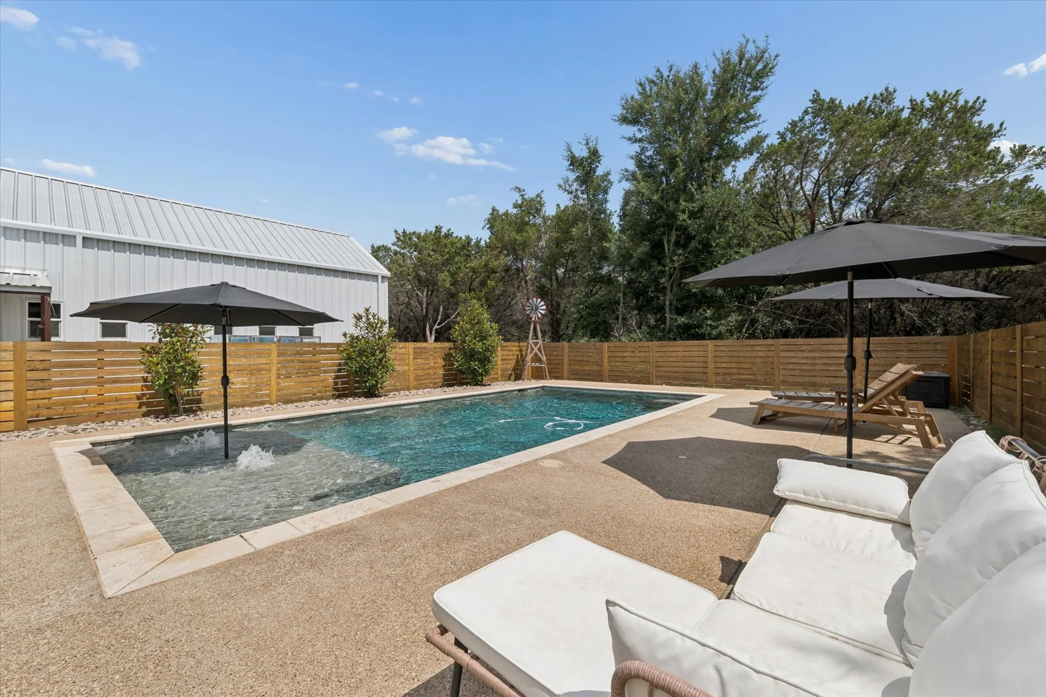 Rectangular swimming pool featuring a tanning ledge with umbrella stand and water feature, surrounded by a gravel aggregate patio