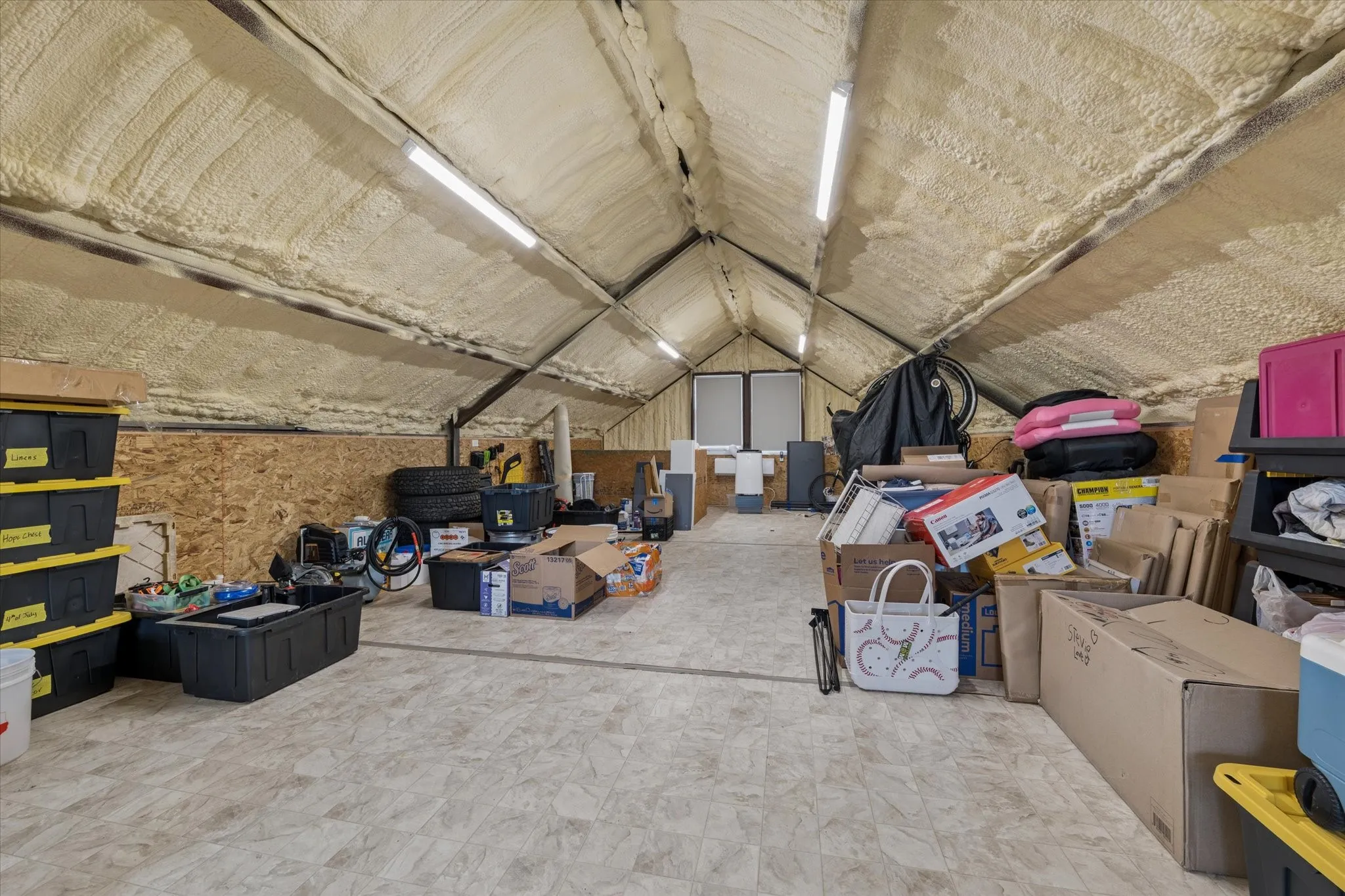 Attic space featuring spray foam insulation, exposed structural beams, and a durable plywood floor