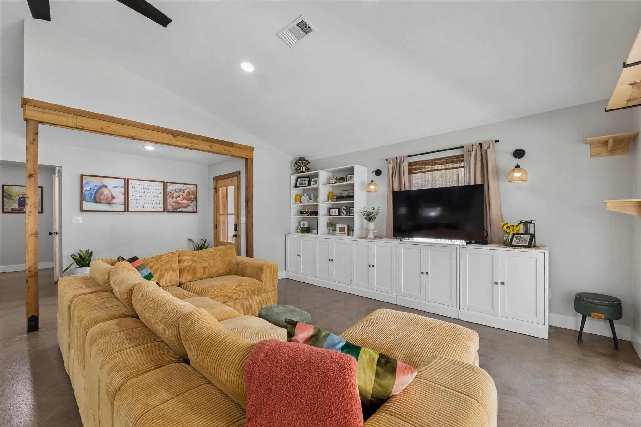 Spacious living area featuring high vaulted ceilings, recessed lighting, concrete flooring, and a built-in entertainment center with open shelving and cabinet storage