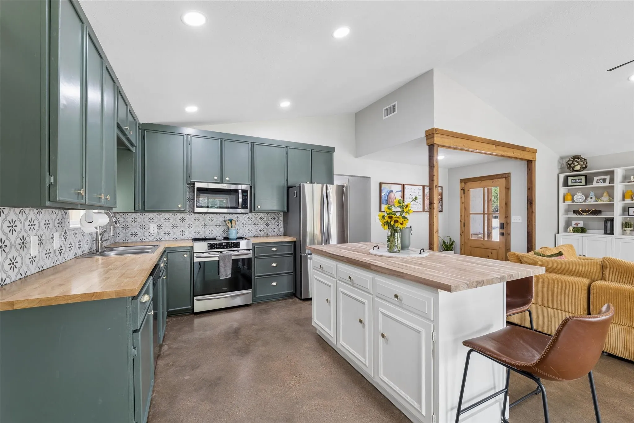 Open-concept kitchen featuring stained concrete flooring, recessed lighting, and a white island with a wood-finish countertop