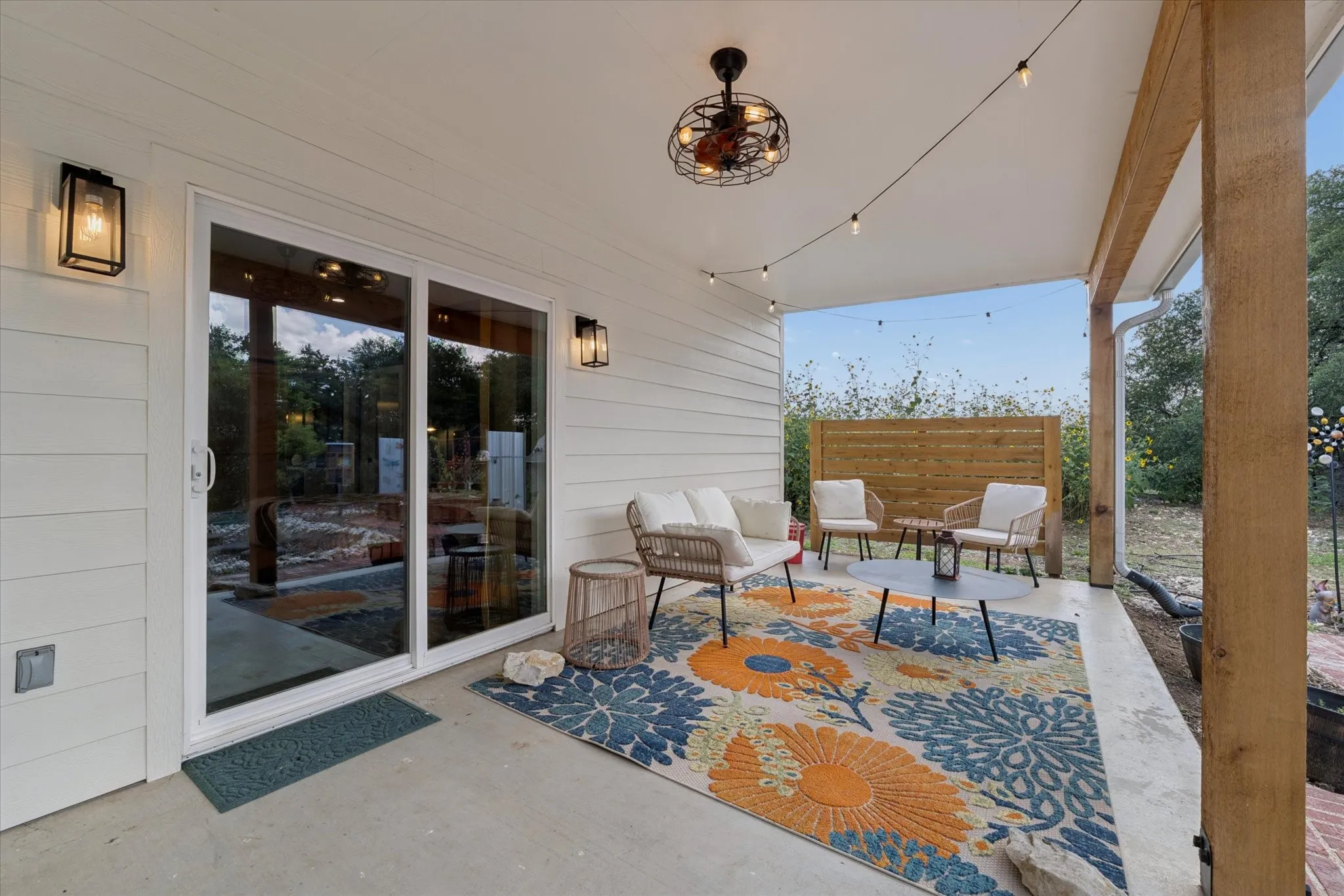 Covered patio featuring a ceiling fan with integrated lighting, string lights, and a wood privacy fence