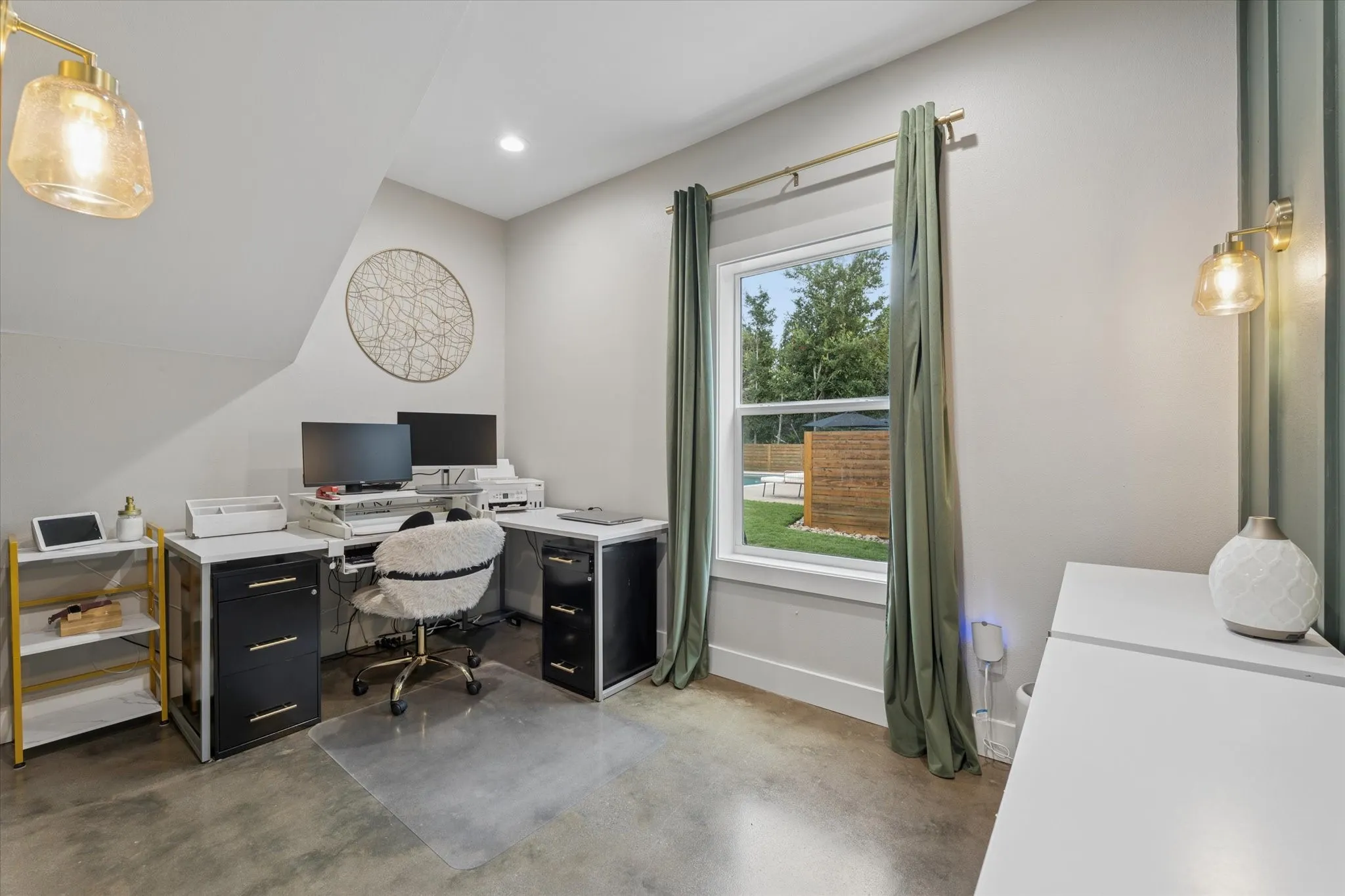 Versatile interior space featuring polished concrete flooring, a double-hung window with exterior landscape, built-in recessed lighting, and wall-mounted sconces