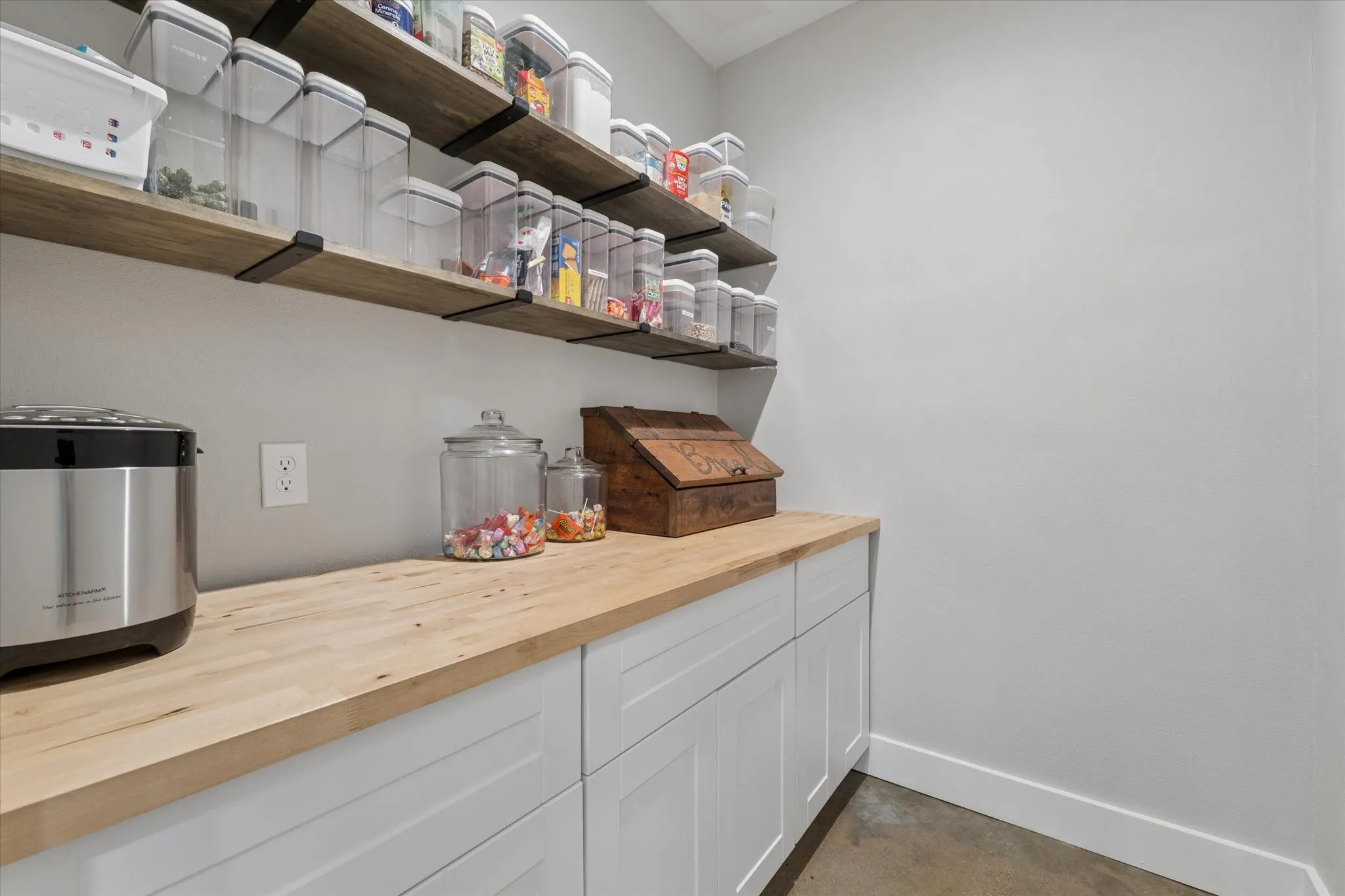 Pantry featuring extensive wood-finish shelving with black metal supports, white shaker-style cabinetry, and a natural wood-finish countertop