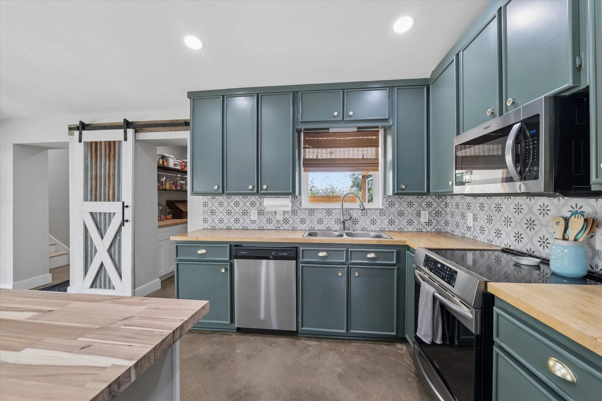 Modern kitchen featuring teal cabinetry, wood-finish countertops, stainless steel appliances, and a patterned tile backsplash