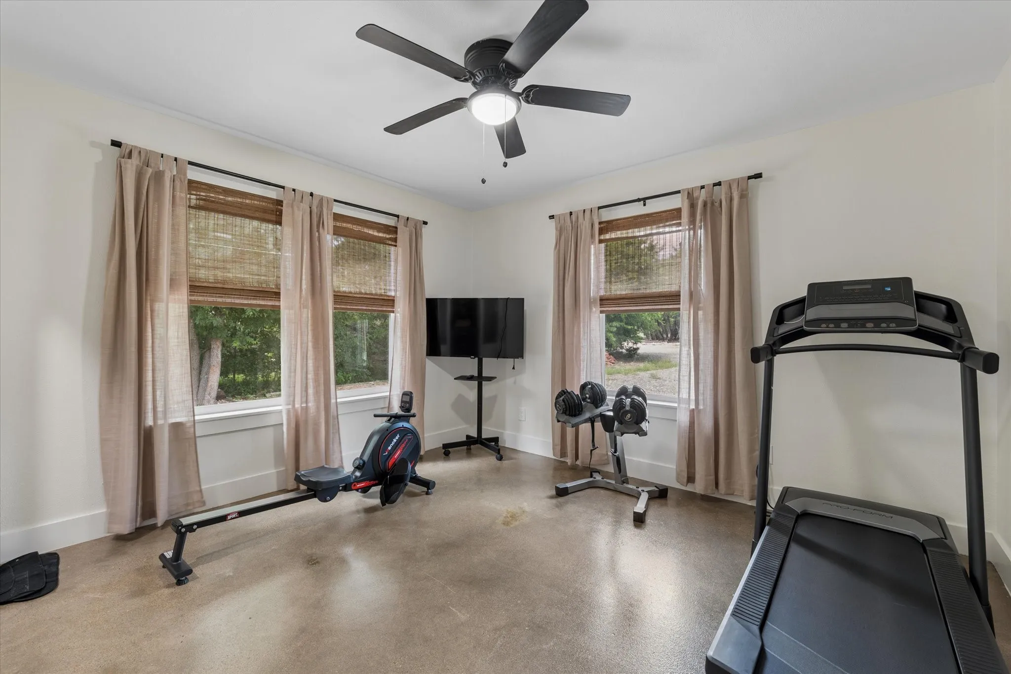 Versatile bonus room featuring a ceiling fan with integrated lighting, polished concrete flooring, and multiple windows with woven wood blinds and drapery