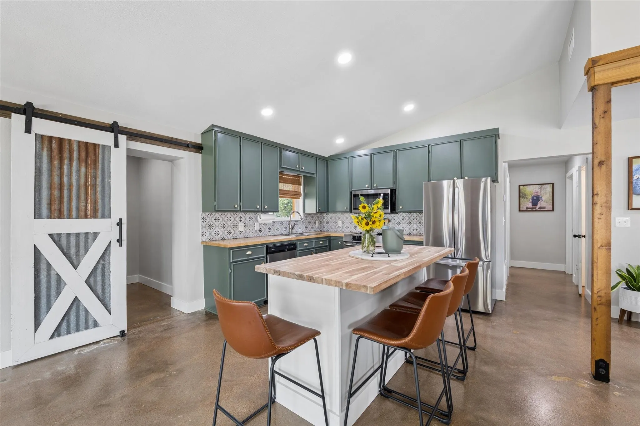 Open-concept kitchen featuring sage green cabinetry, a patterned tile backsplash, stainless steel appliances, and a central island with a wood-finish countertop