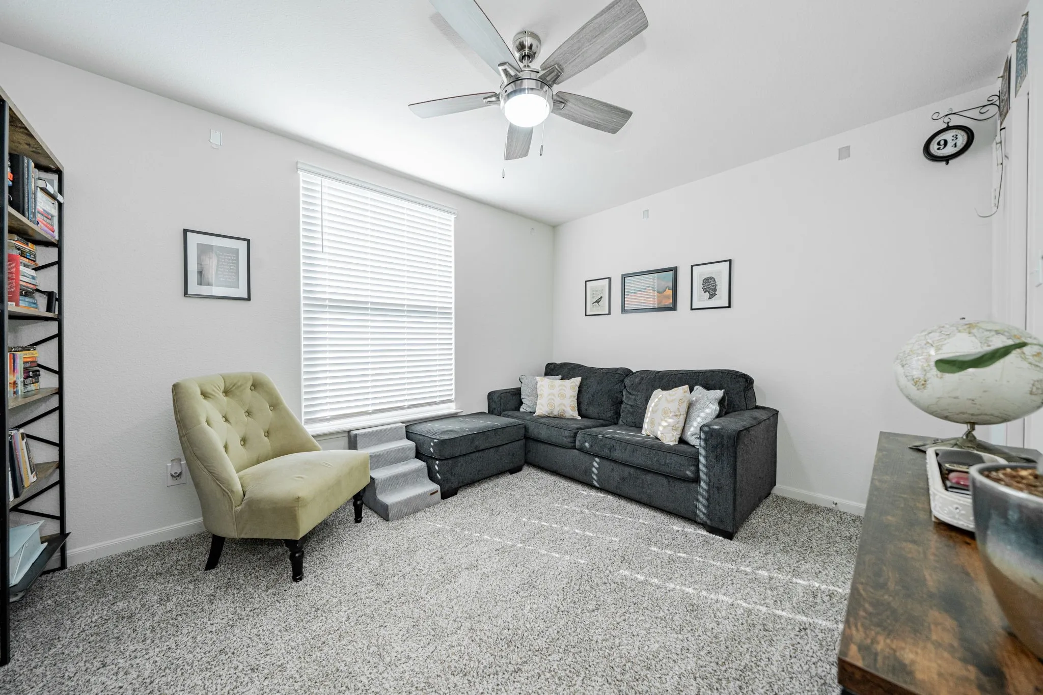 Carpeted interior space featuring a ceiling fan with integrated lighting, a large window with blinds, and white walls