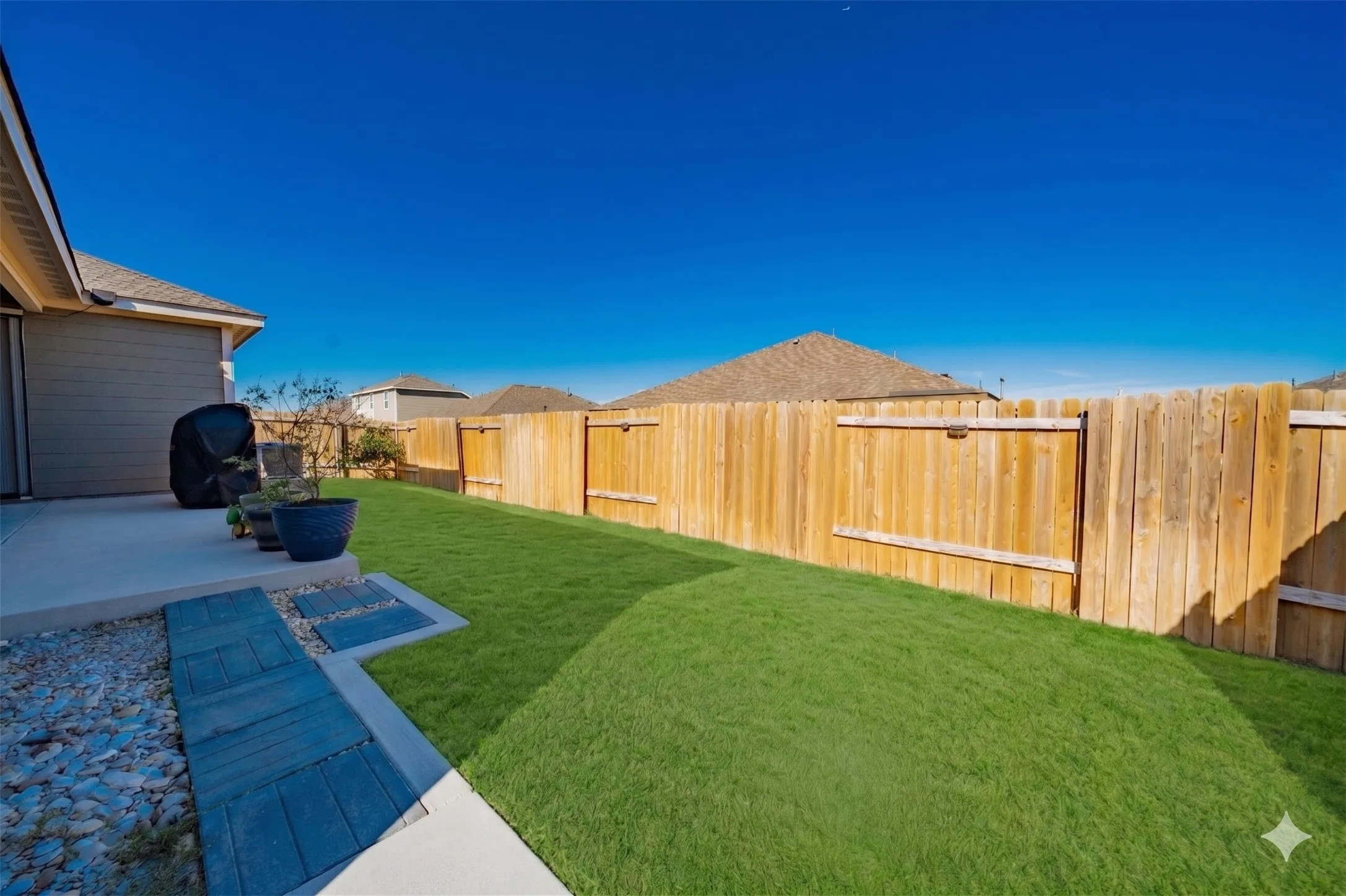 Private backyard featuring a concrete patio, a wooden privacy fence, and a lush green lawn