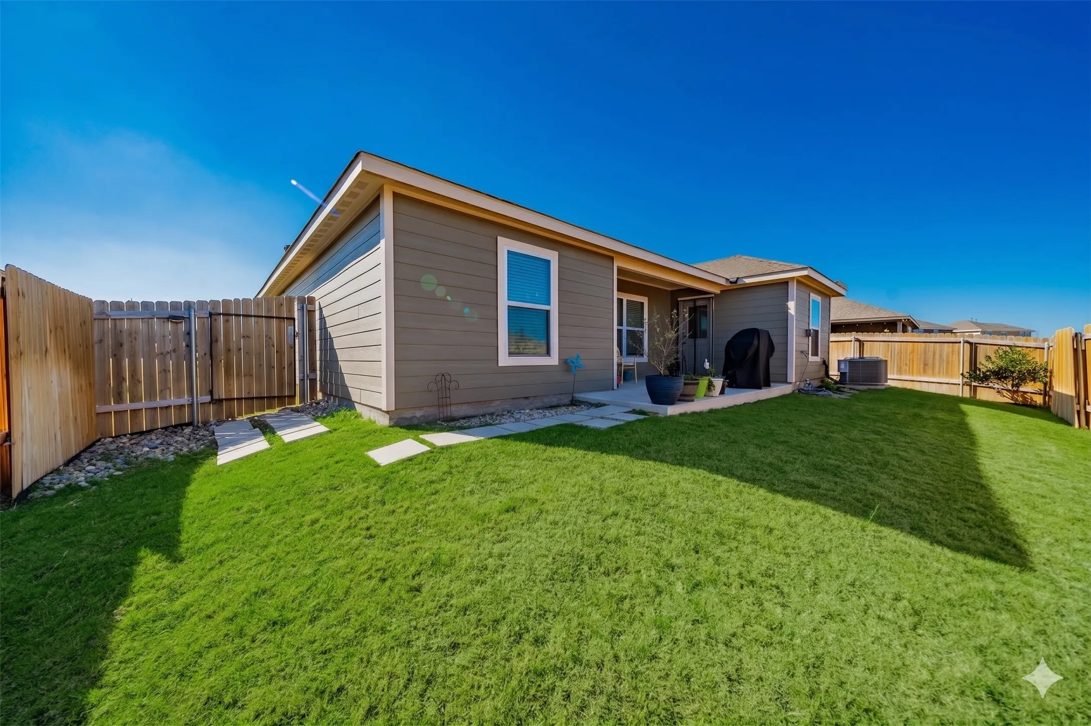 Expansive backyard featuring a lush lawn, privacy fencing, a concrete patio, and stepping stones leading to a gated side yard