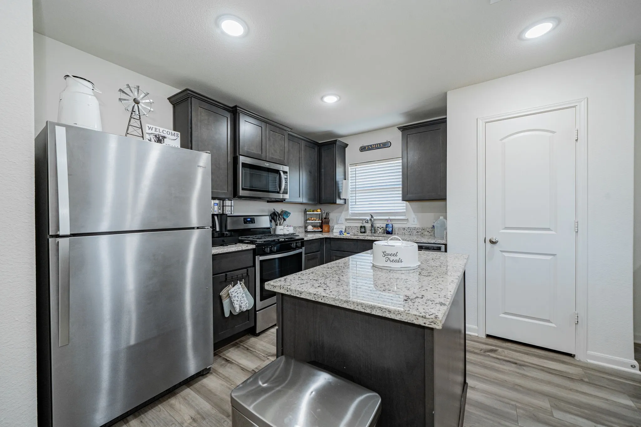 Kitchen featuring dark wood-finish cabinetry, stainless steel appliances, a center island with a light-toned stone countertop, and wood-finish flooring
