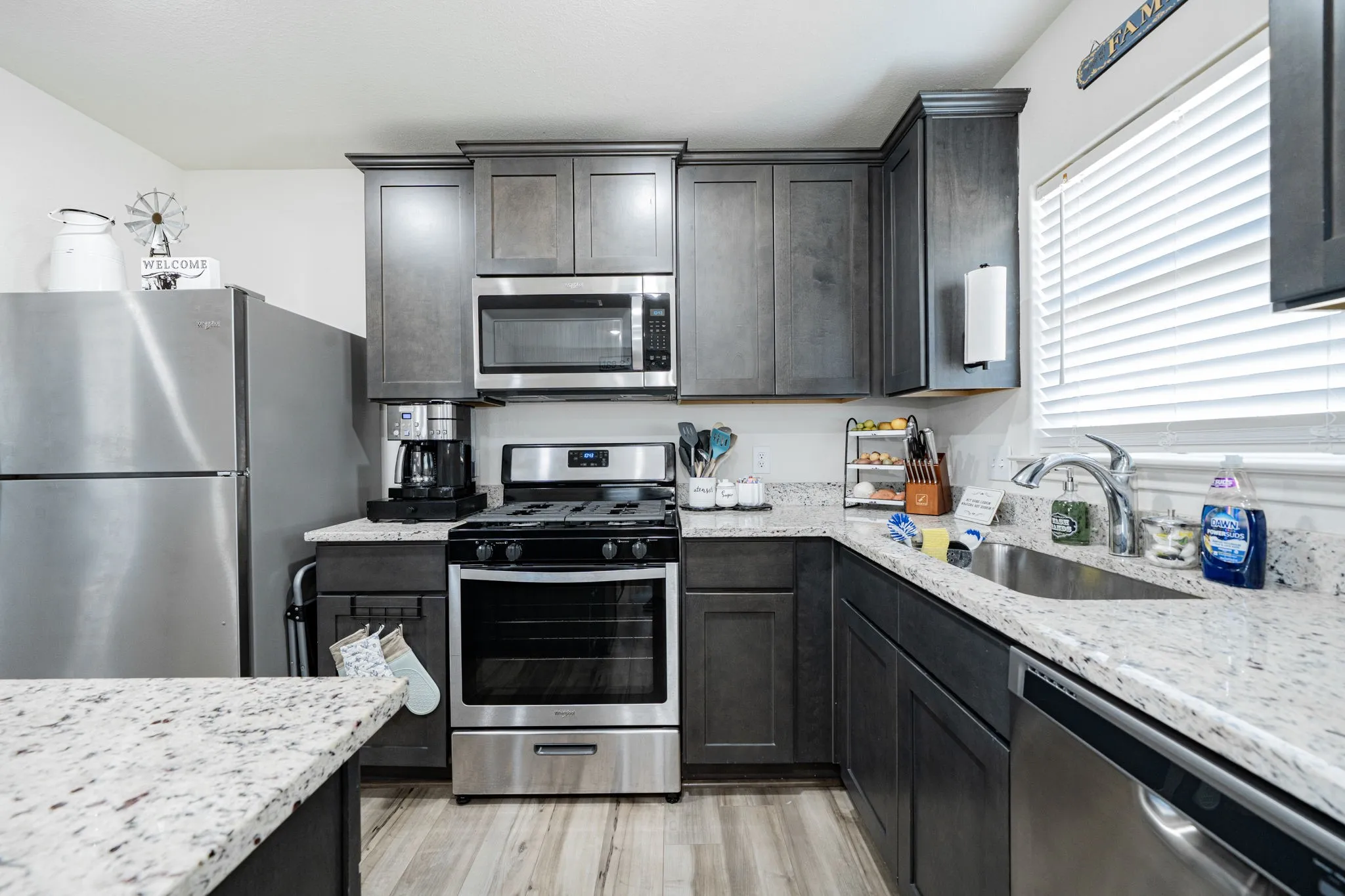 Modern kitchen featuring dark wood-finish cabinetry, light speckled countertops, stainless steel appliances, and wood-finish flooring