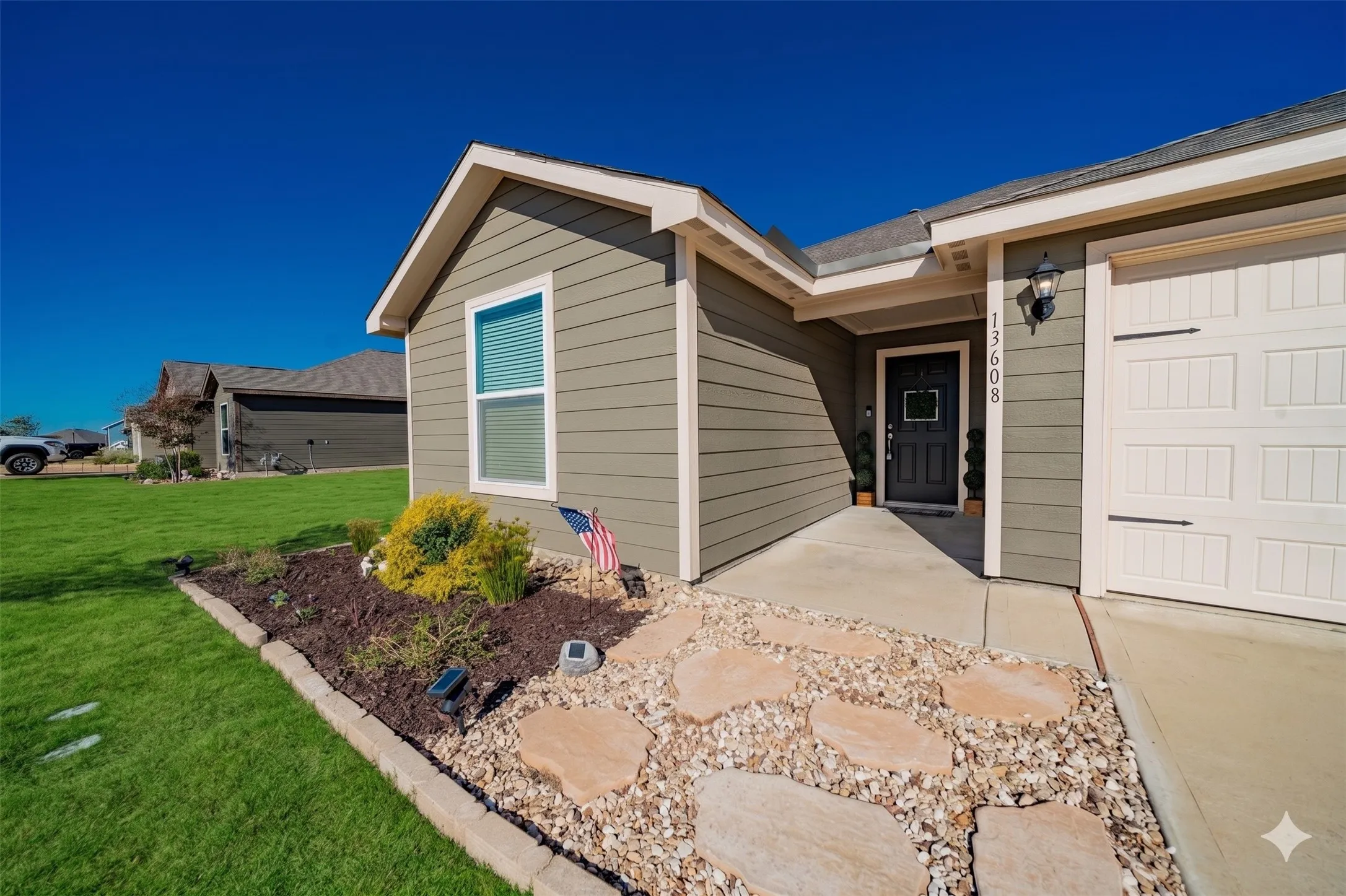 Front exterior featuring horizontal siding, an attached garage, a concrete pathway, a landscaped rock garden, and a green lawn
