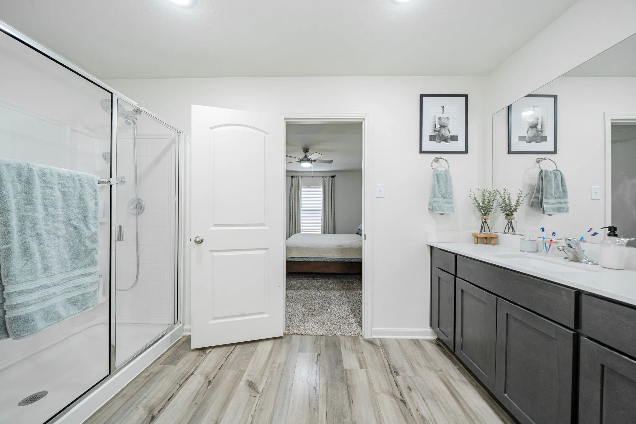 Bathroom featuring wood-finish flooring, a glass-enclosed shower, a double vanity with dark cabinetry, and integrated lighting