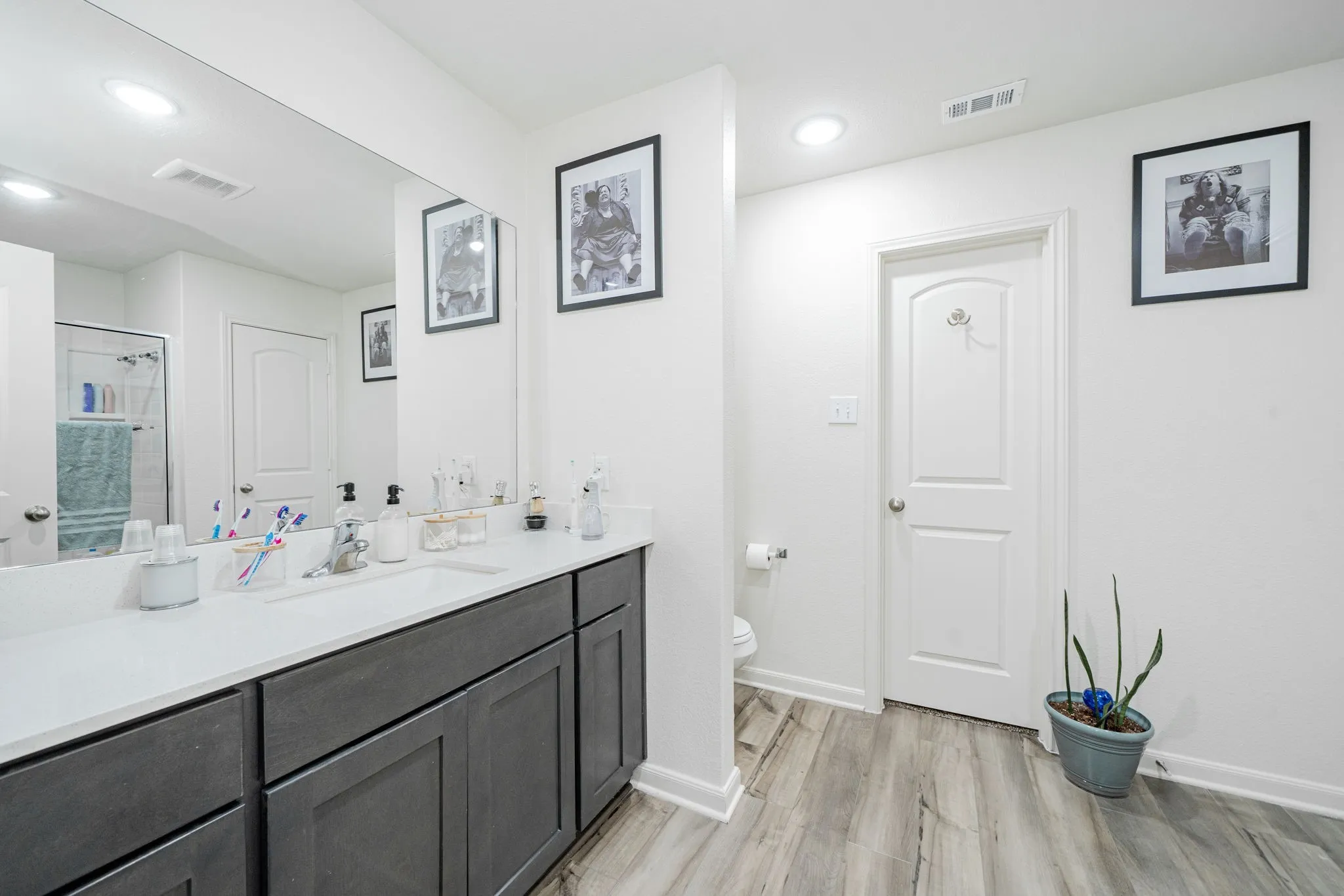Bathroom featuring a spacious dual vanity with a white countertop and dark wood-finish cabinetry, a large wall-mounted mirror, wood-finish flooring, and recessed lighting