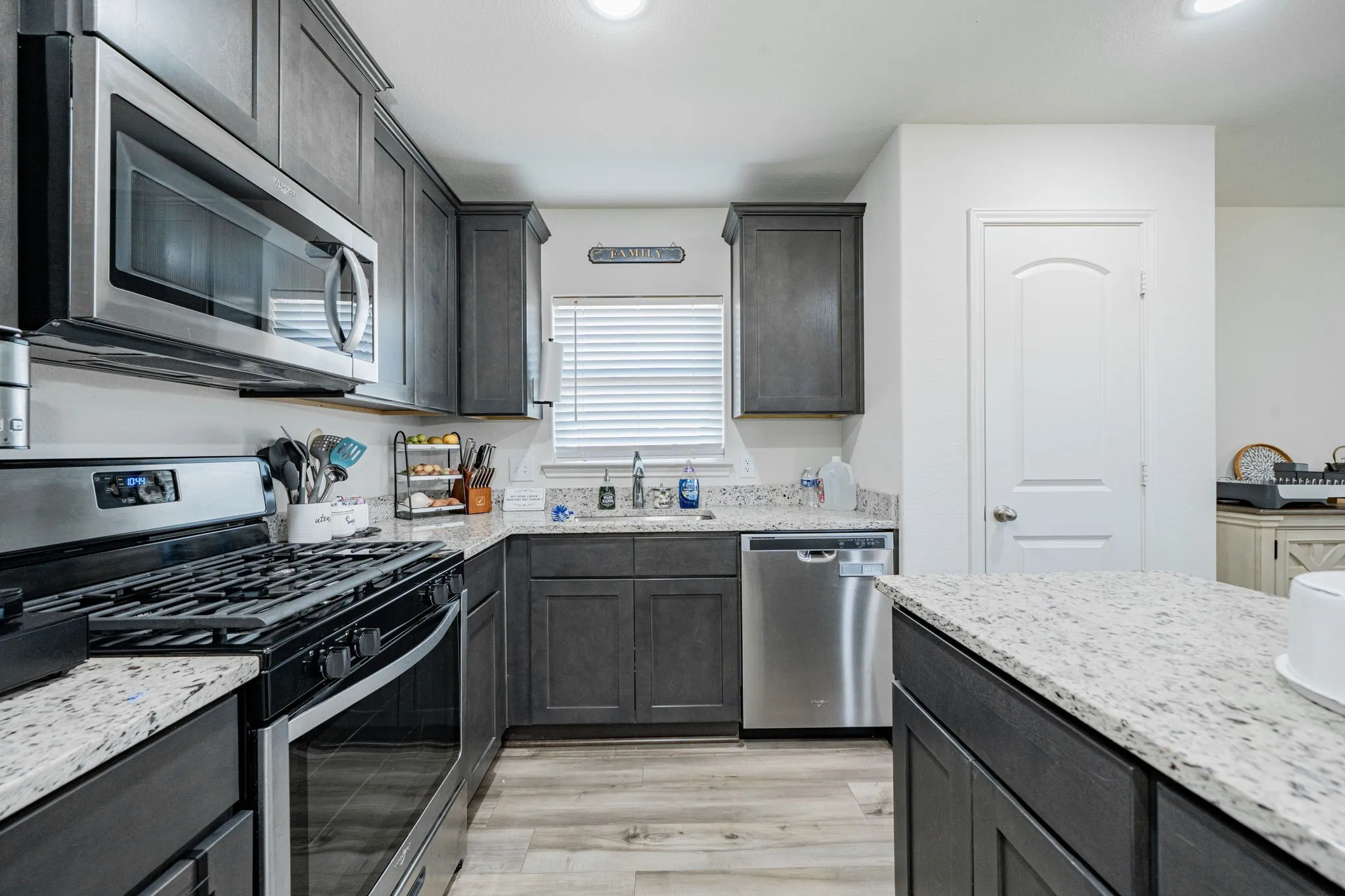 Kitchen featuring dark-stained cabinetry, stainless steel appliances, speckled countertops, wood-finish flooring, and a central island