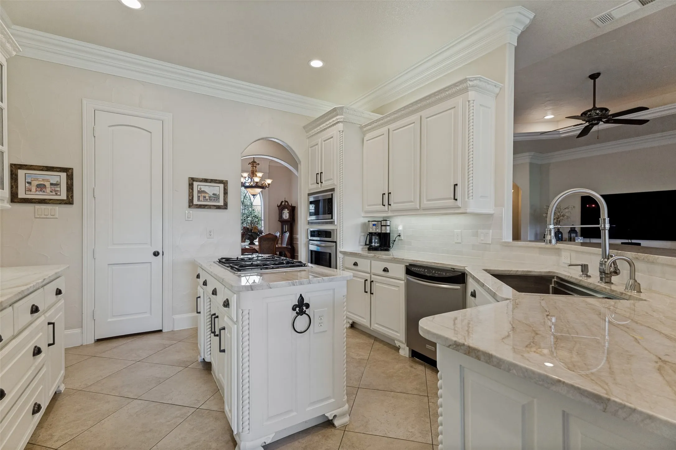 Gourmet kitchen featuring a central island with built-in cooktop, extensive white cabinetry, light-toned stone countertops, and tile flooring