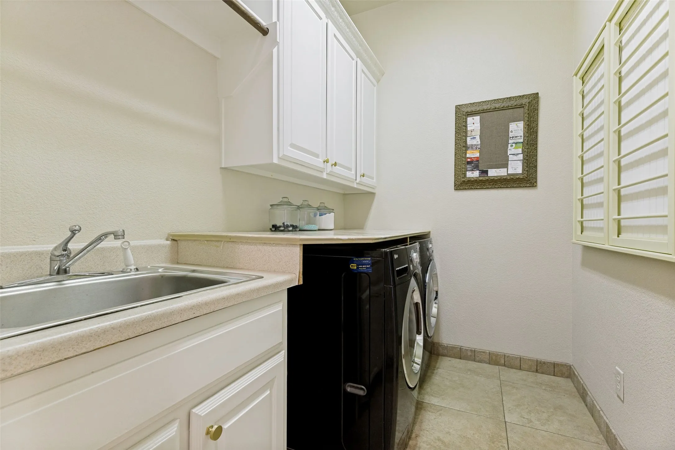 Utility room featuring a built-in sink with a countertop, white cabinetry with gold-tone hardware, and tile flooring