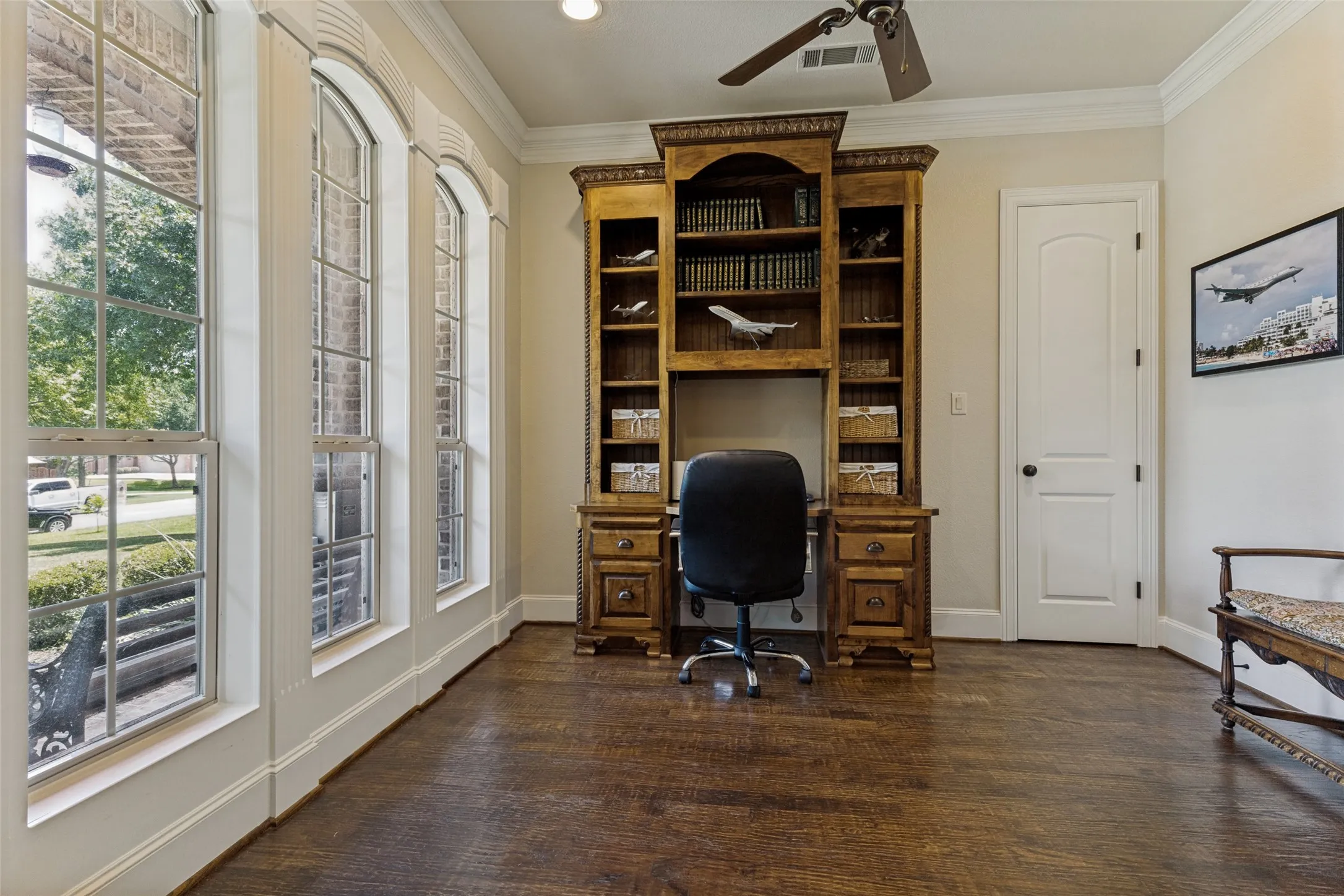 Hardwood flooring throughout featuring a built-in wooden desk and shelving unit, crown molding, and a ceiling fan