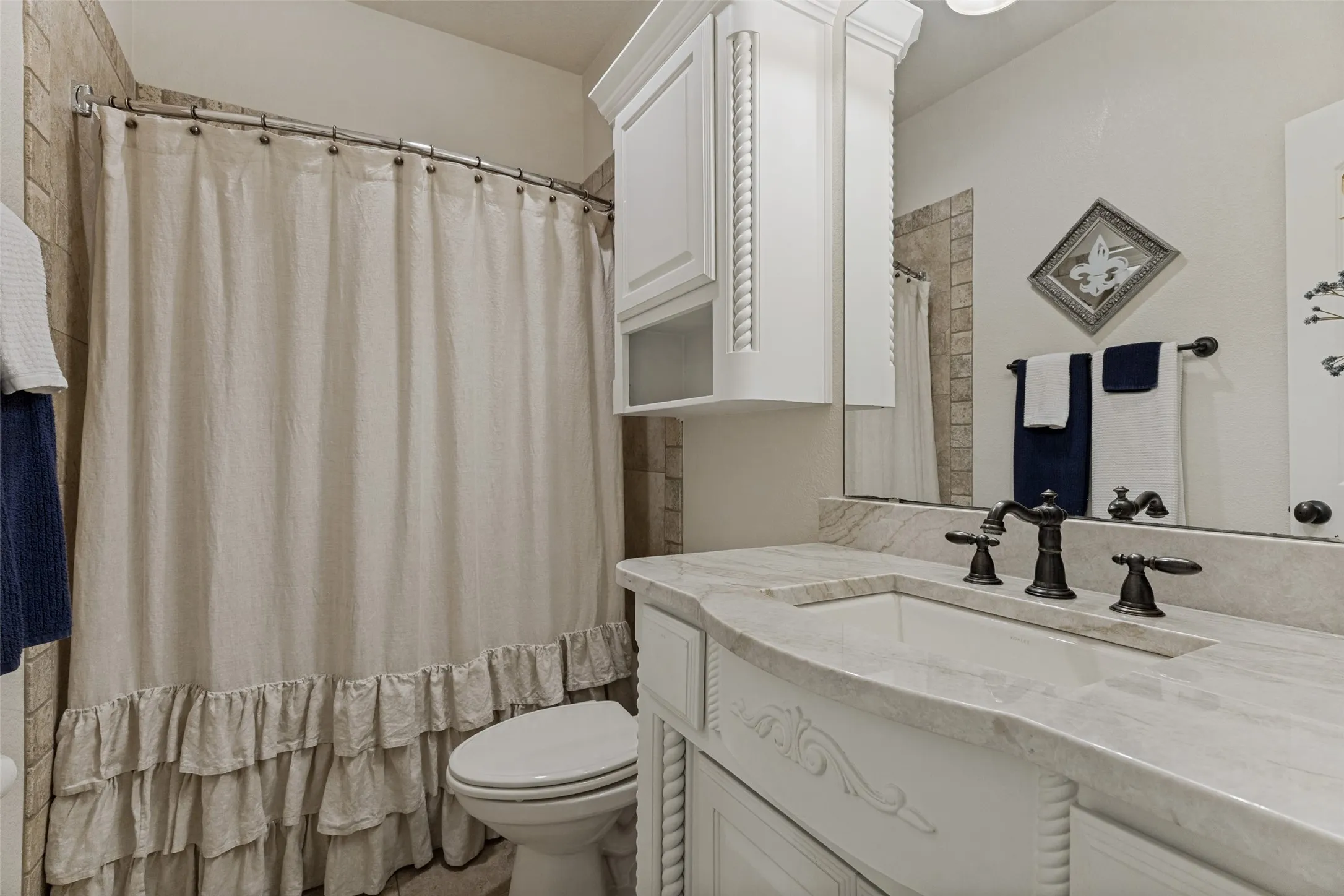 Bathroom featuring a built-in vanity with a light-toned countertop and integrated sink, dark-toned faucet, wall-mounted mirror, and white cabinetry