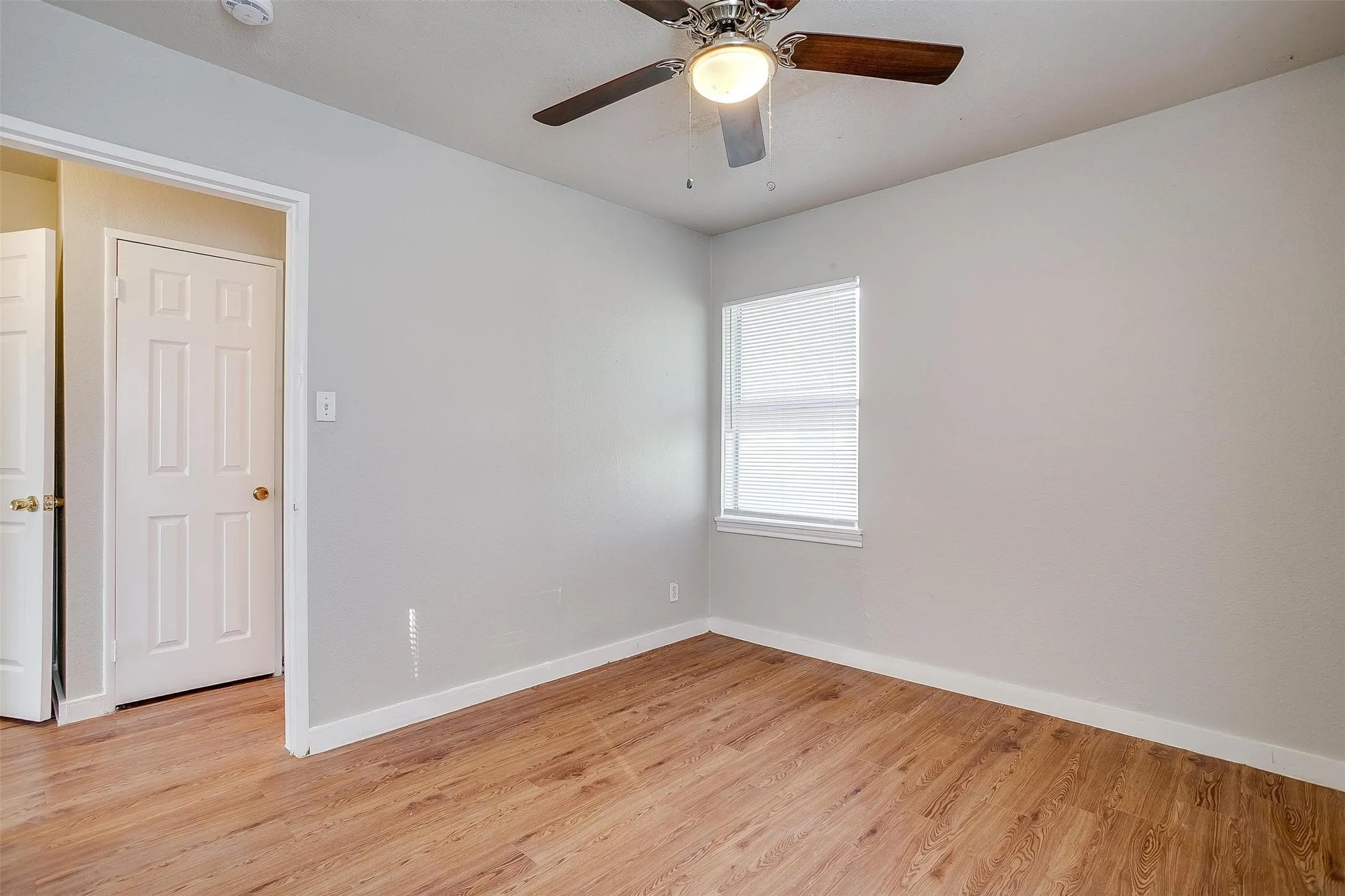 Room featuring wood-finish flooring, a ceiling fan with light, a window with blinds, and light-toned wall finishes