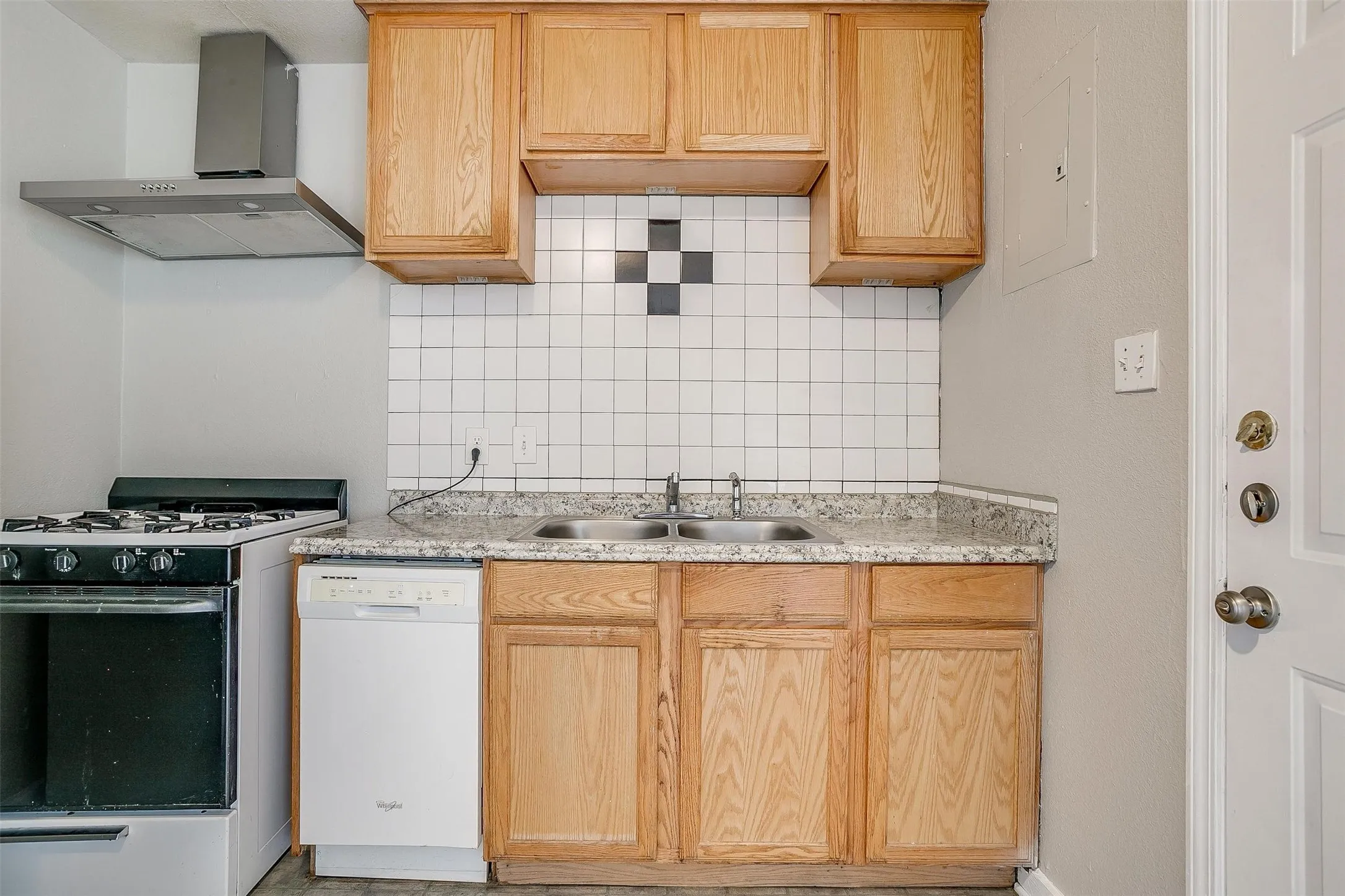 Kitchen featuring wood cabinetry, a double basin stainless steel sink, and a white tile backsplash with decorative accents