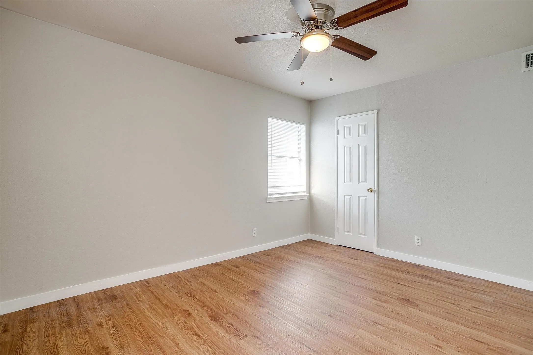 Spacious room featuring wood-finish flooring, light gray walls, white trim, a ceiling fan with light fixture, and a window with blinds