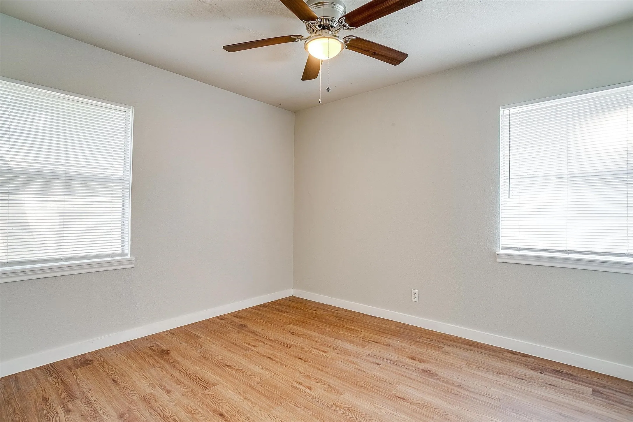 Room featuring wood-finish flooring, light gray walls, a ceiling fan with integrated lighting, and two windows with white blinds