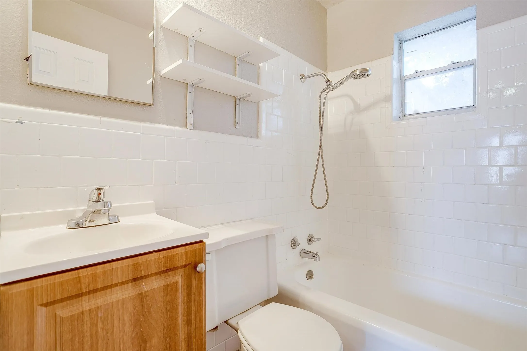 Bathroom featuring a wood-finish vanity with an integrated sink, white subway tile surround, built-in shelving, and a shower/tub combination with a handheld shower head