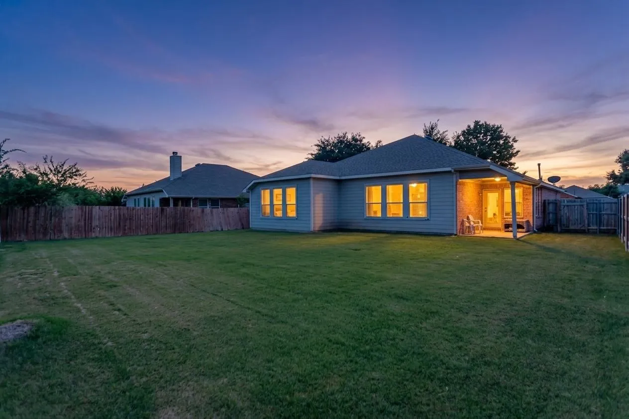 Expansive backyard featuring a manicured lawn, full privacy fencing, and a covered patio with brick columns