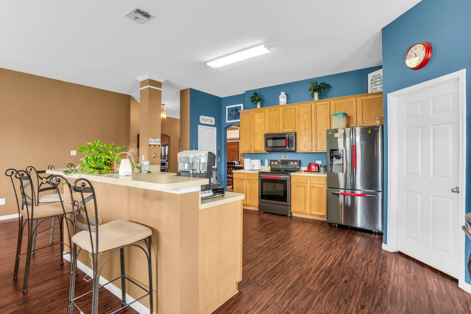 Kitchen featuring wood-finish flooring, light wood cabinetry, stainless steel appliances, and a breakfast bar with a light-toned countertop
