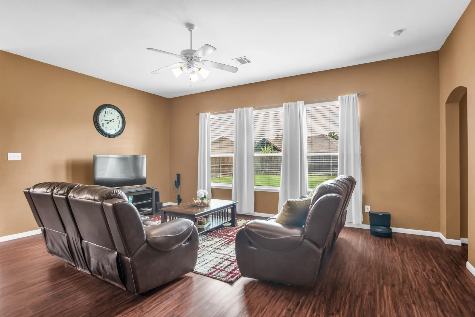 Living area featuring wood-finish flooring, a ceiling fan with light fixture, and an arched entryway