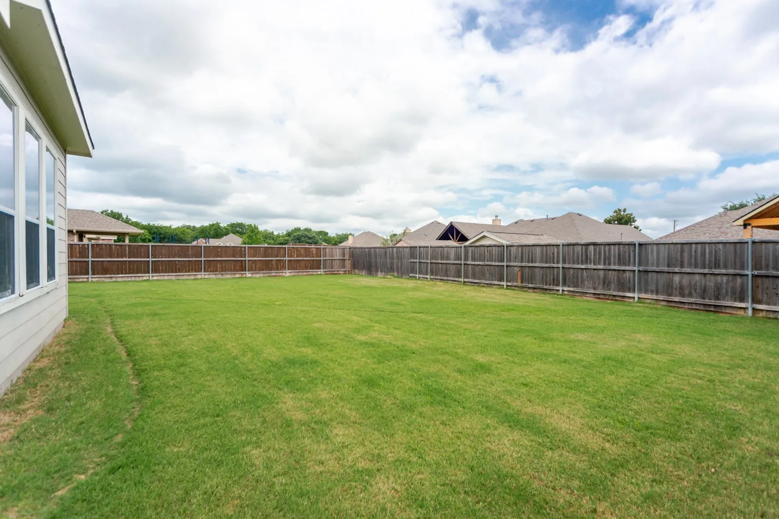 Expansive backyard featuring a lush lawn, privacy fencing, and a neutral-toned exterior wall with multiple windows