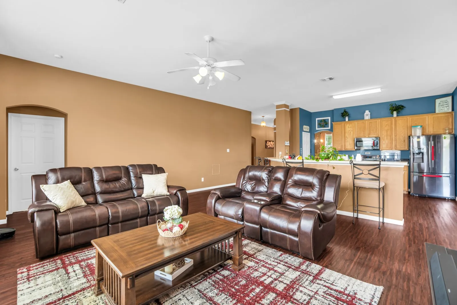 Open-concept living space featuring wood-finish flooring, a ceiling fan with integrated lighting, and an arched doorway
