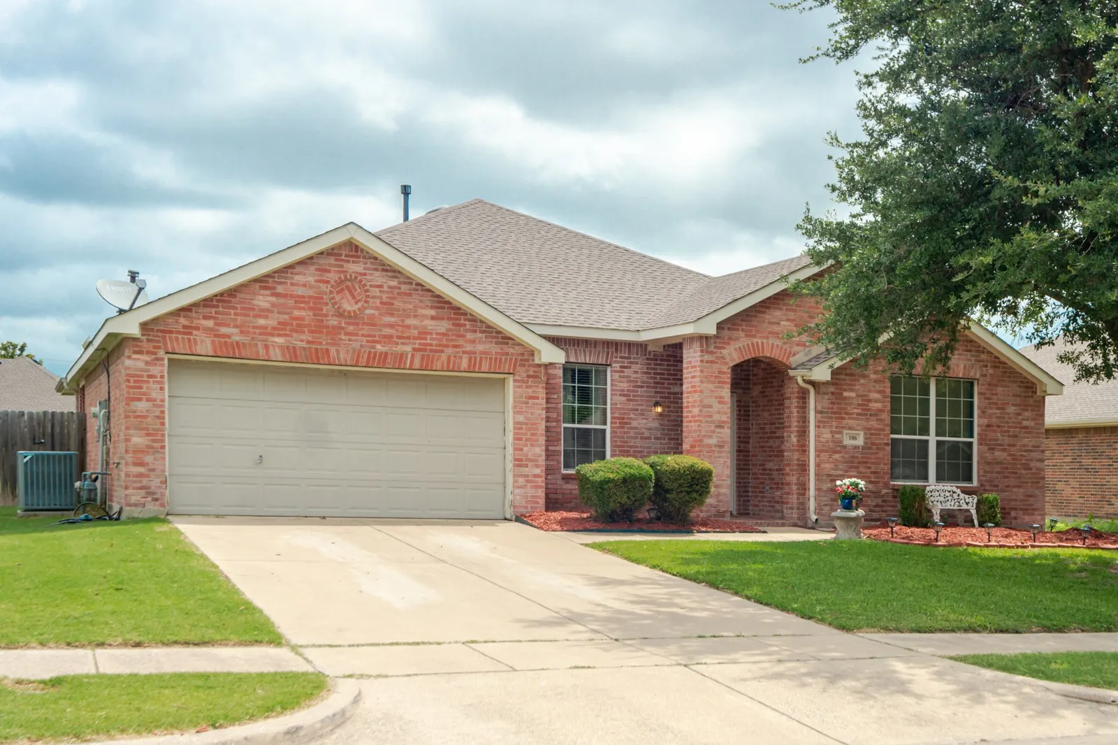 Brick facade residence with a two-car garage, concrete driveway, arched entry, and pitched roof