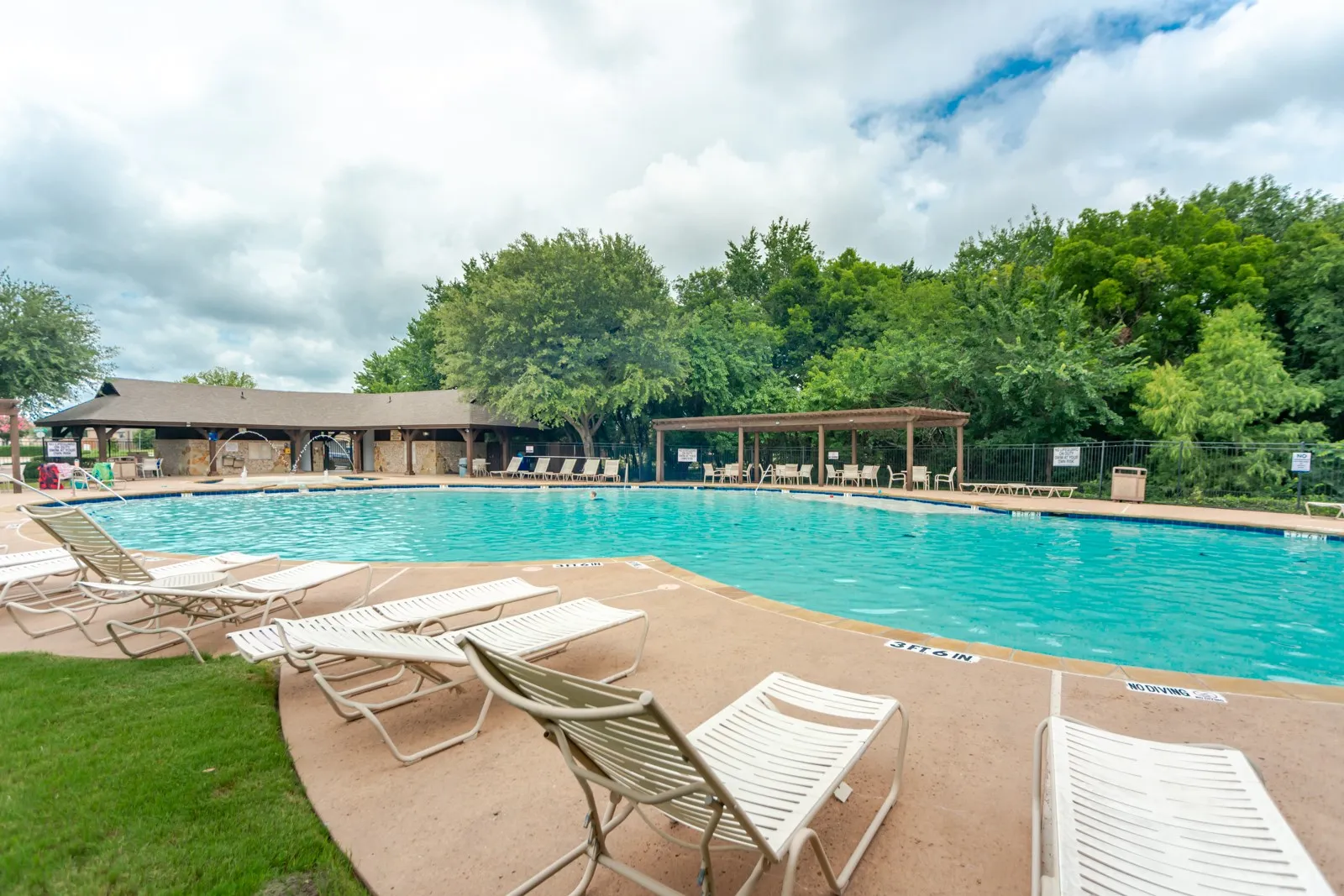 Resort-style swimming pool with extensive concrete decking, surrounded by mature trees