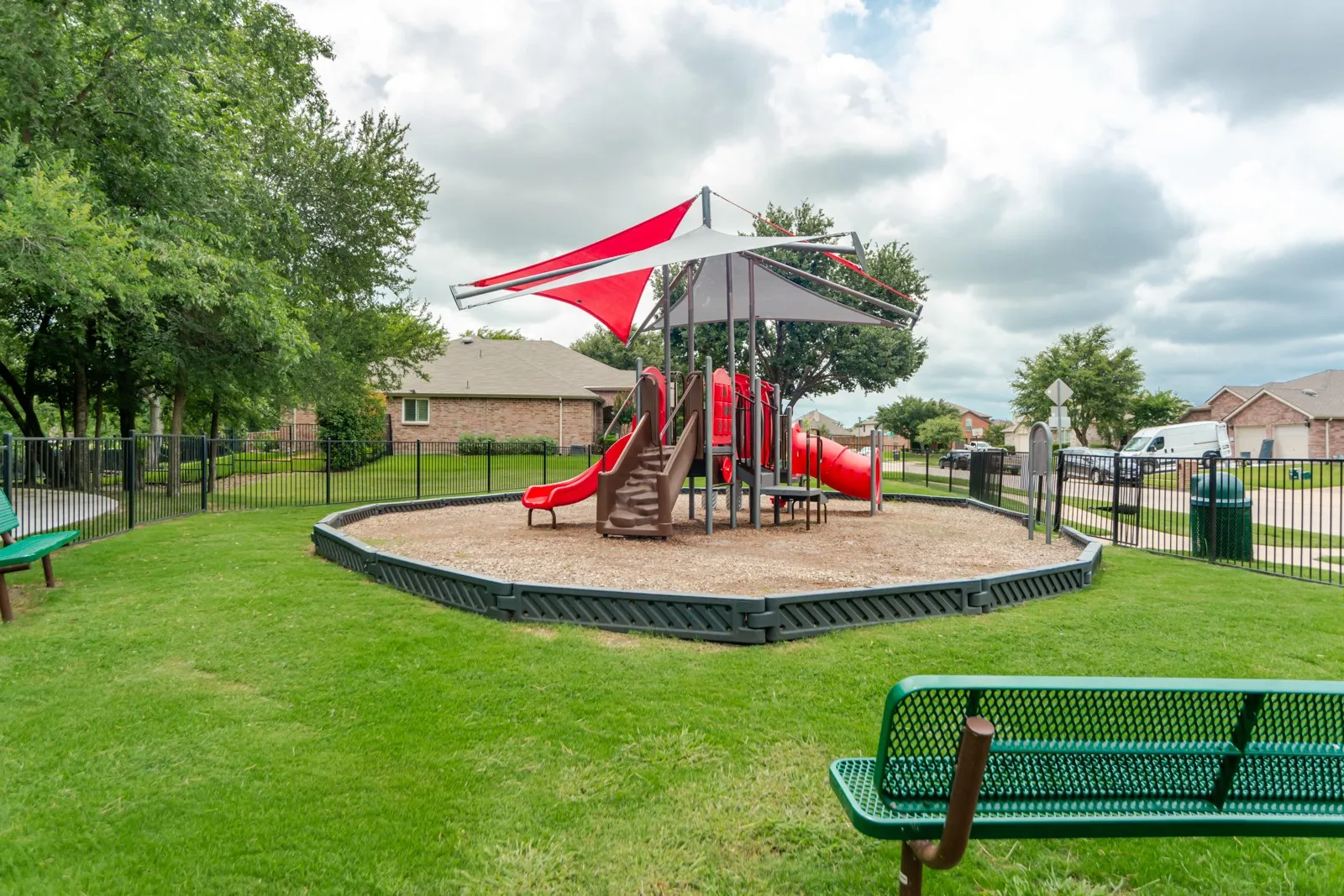 Fenced playground area featuring a play structure with slides and shade canopies