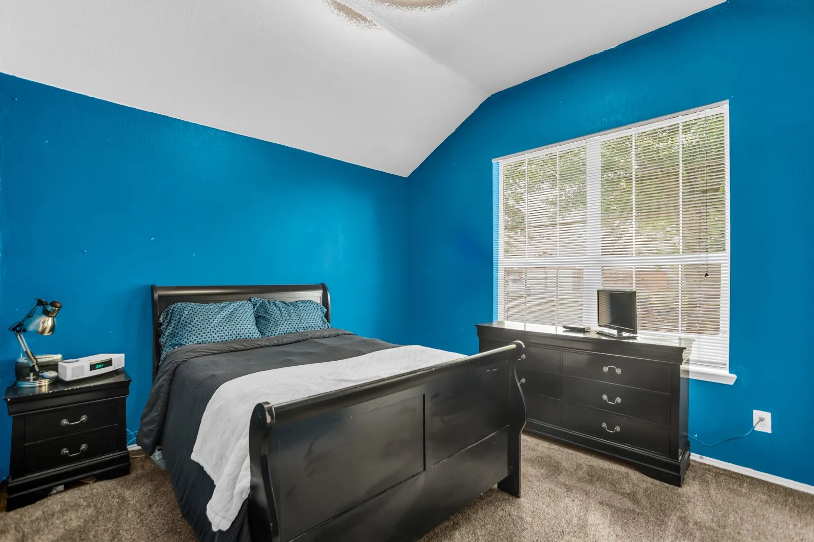 Bedroom with a vaulted ceiling, textured blue walls, and a large window featuring horizontal blinds