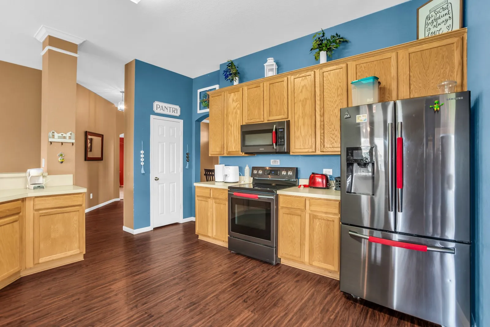 Kitchen featuring wood-finish flooring, light wood cabinetry, light-toned countertops, and a full suite of stainless steel appliances including a refrigerator, range, and microwave