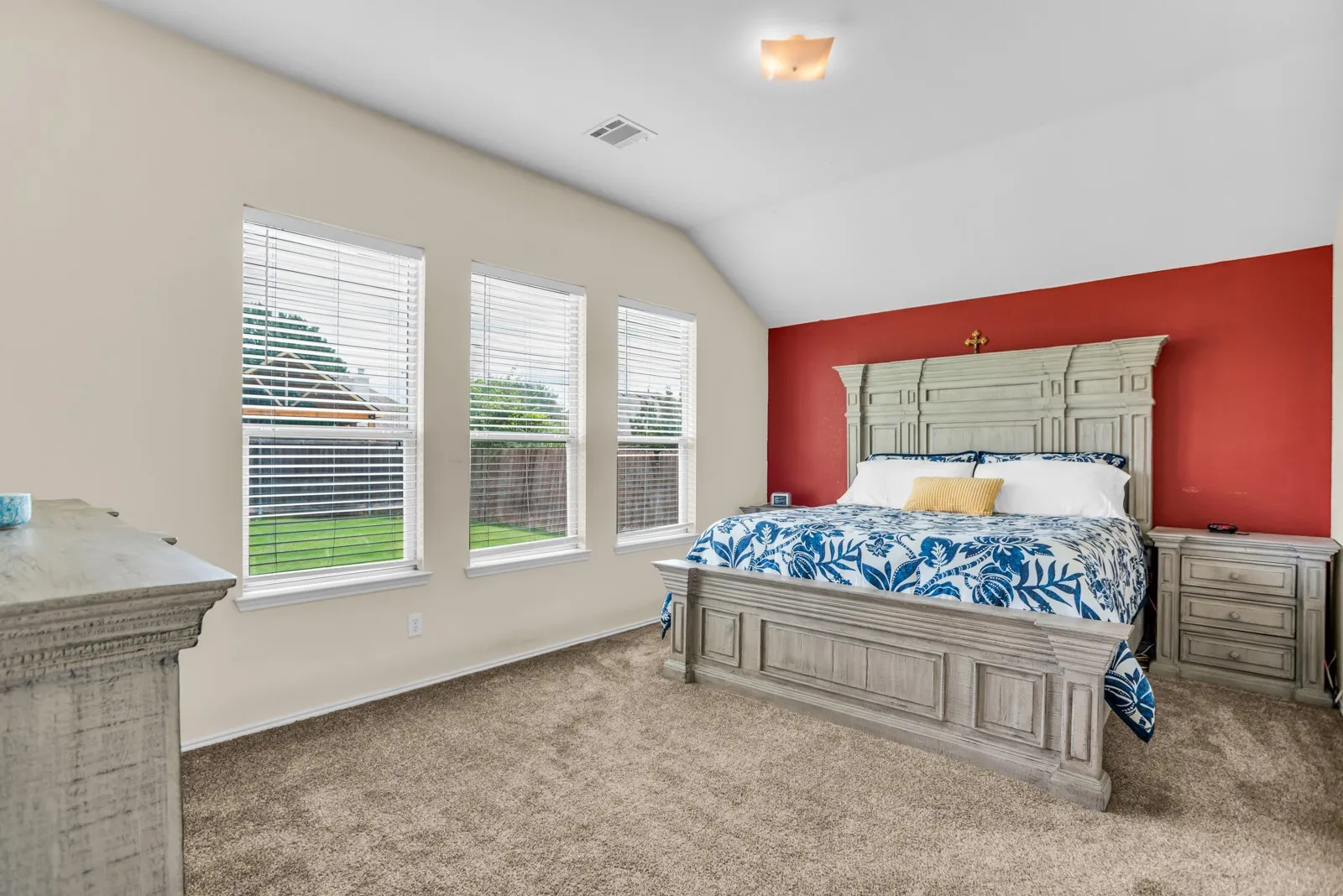 Carpeted room with a vaulted ceiling, a red accent wall, and three windows overlooking a green lawn