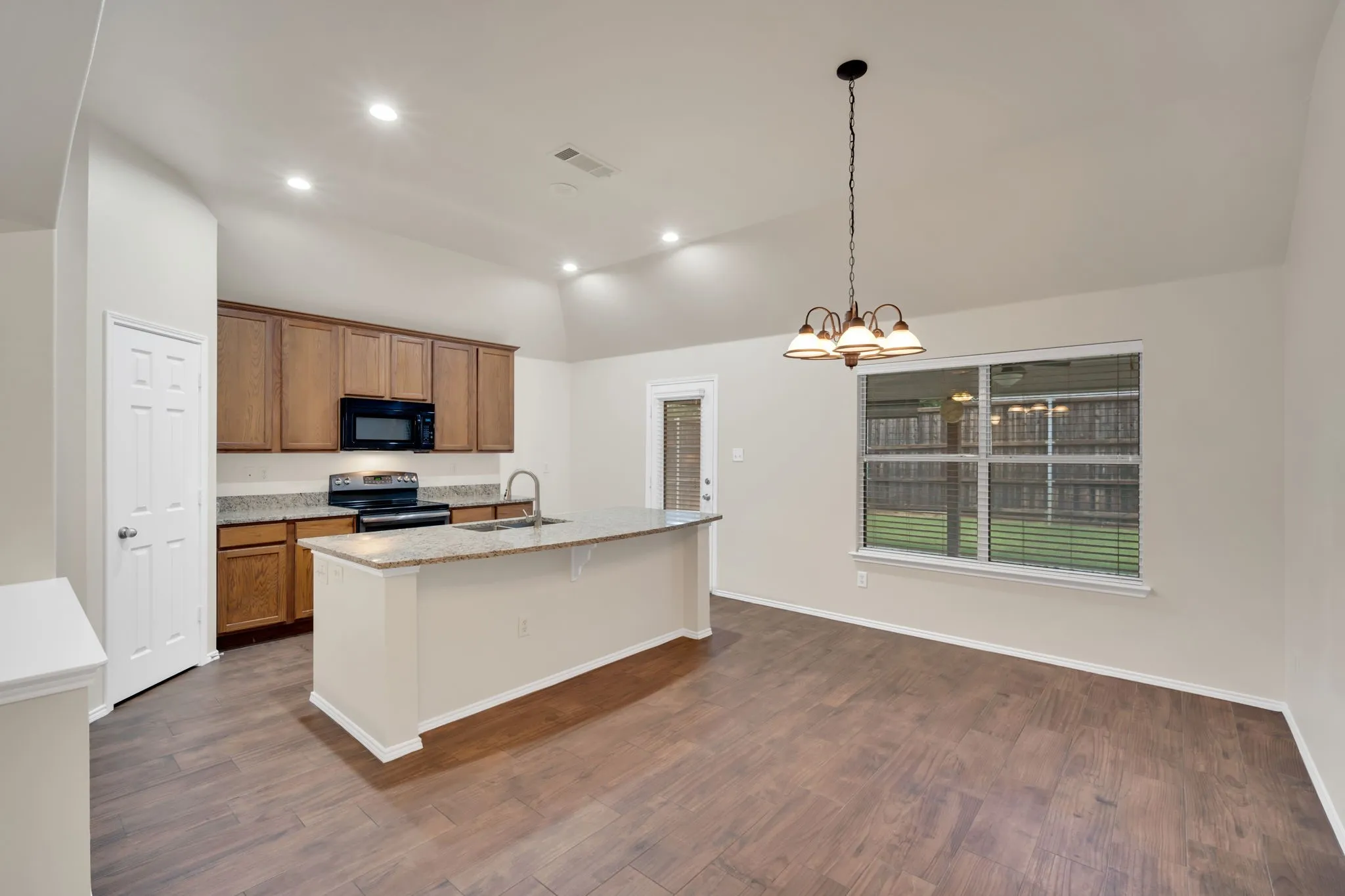 Open-concept kitchen and dining area featuring wood-finish flooring, vaulted ceilings, and recessed lighting