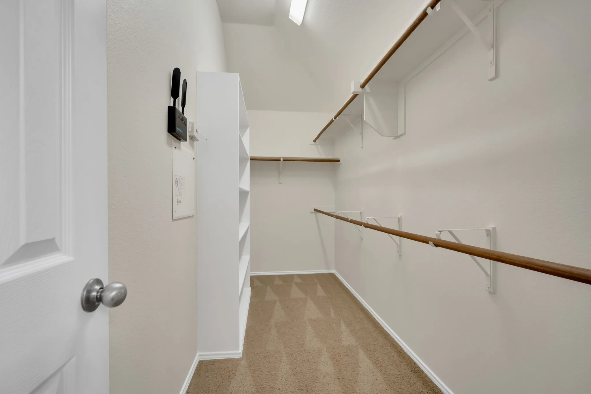 Spacious walk-in closet featuring light beige carpeting, multiple wooden hanging rods, and integrated shelving units