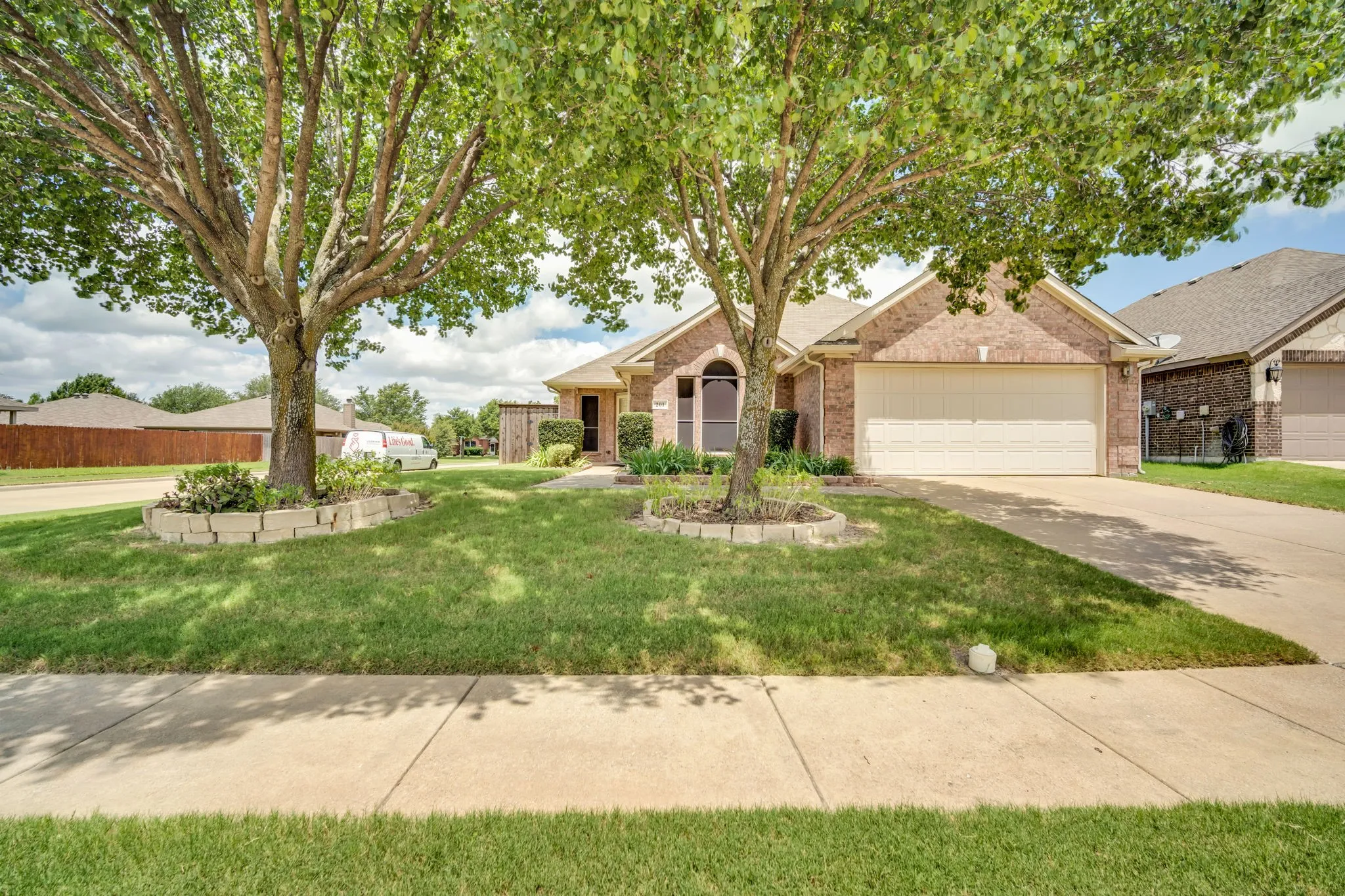 Brick facade home featuring a two-car garage, arched entry, and mature trees