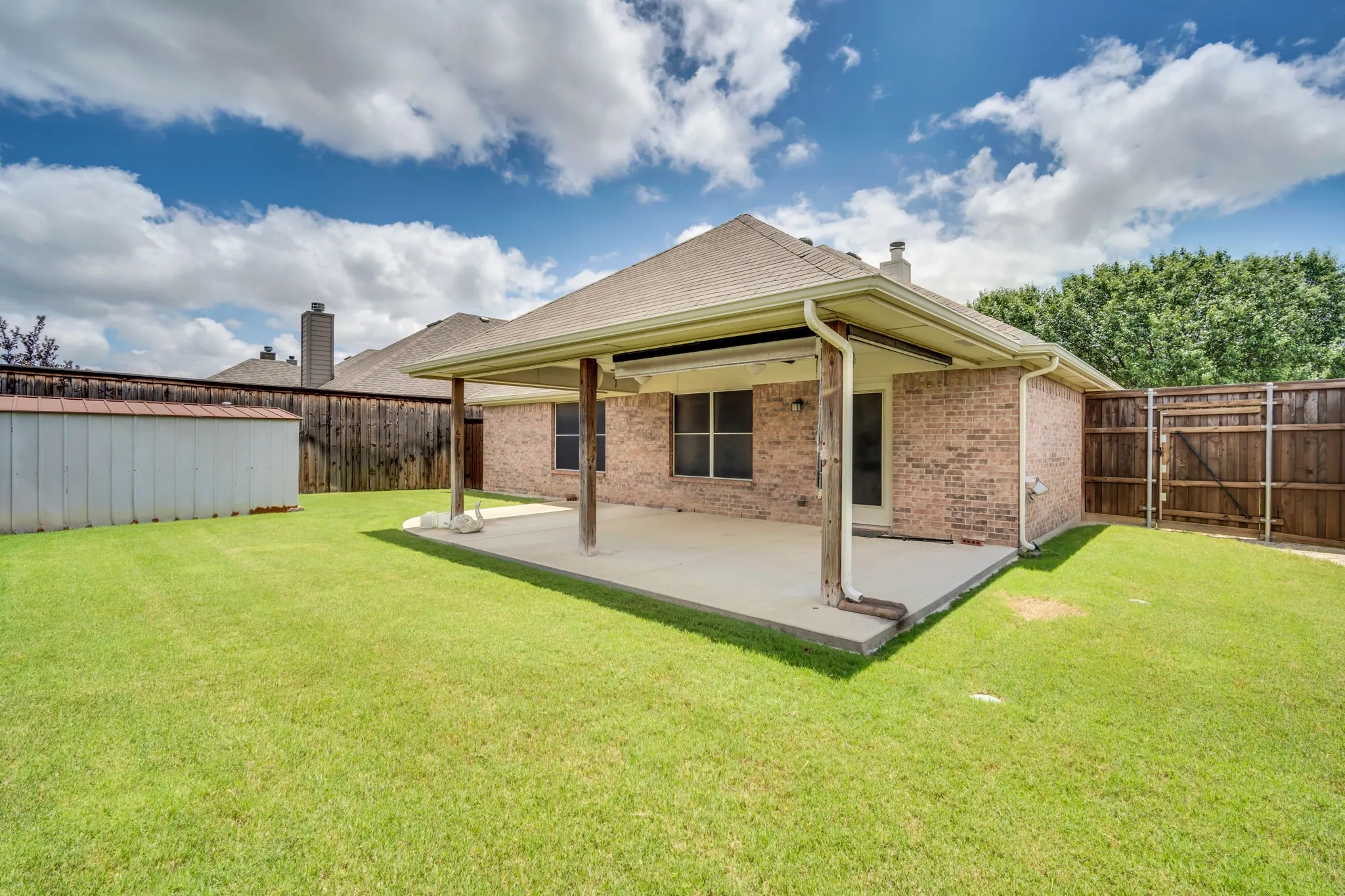 Spacious backyard featuring a covered concrete patio, brick exterior, and an 8ft wood fence