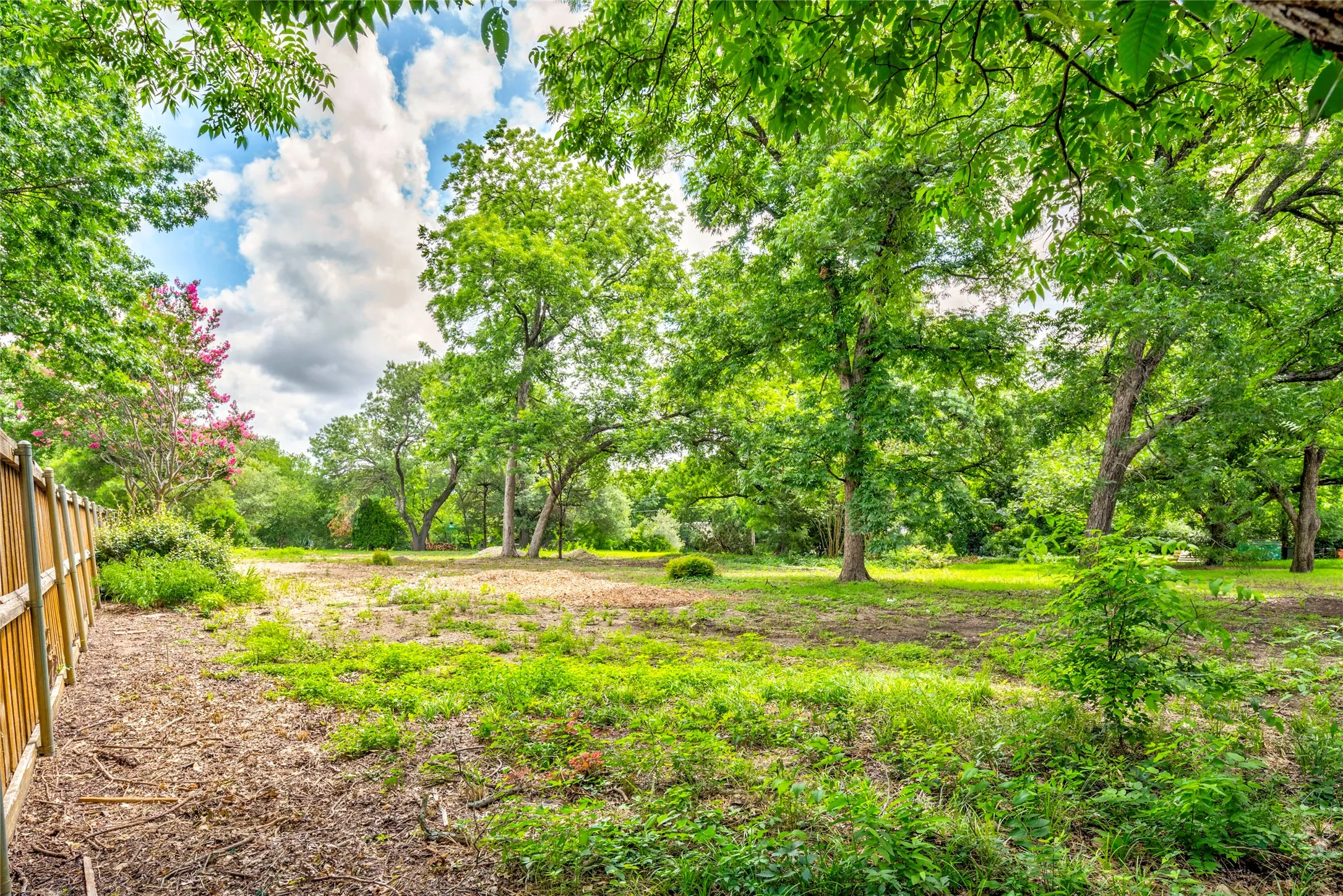 Expansive land parcel featuring mature trees, a partially cleared area, and a wood fence boundary